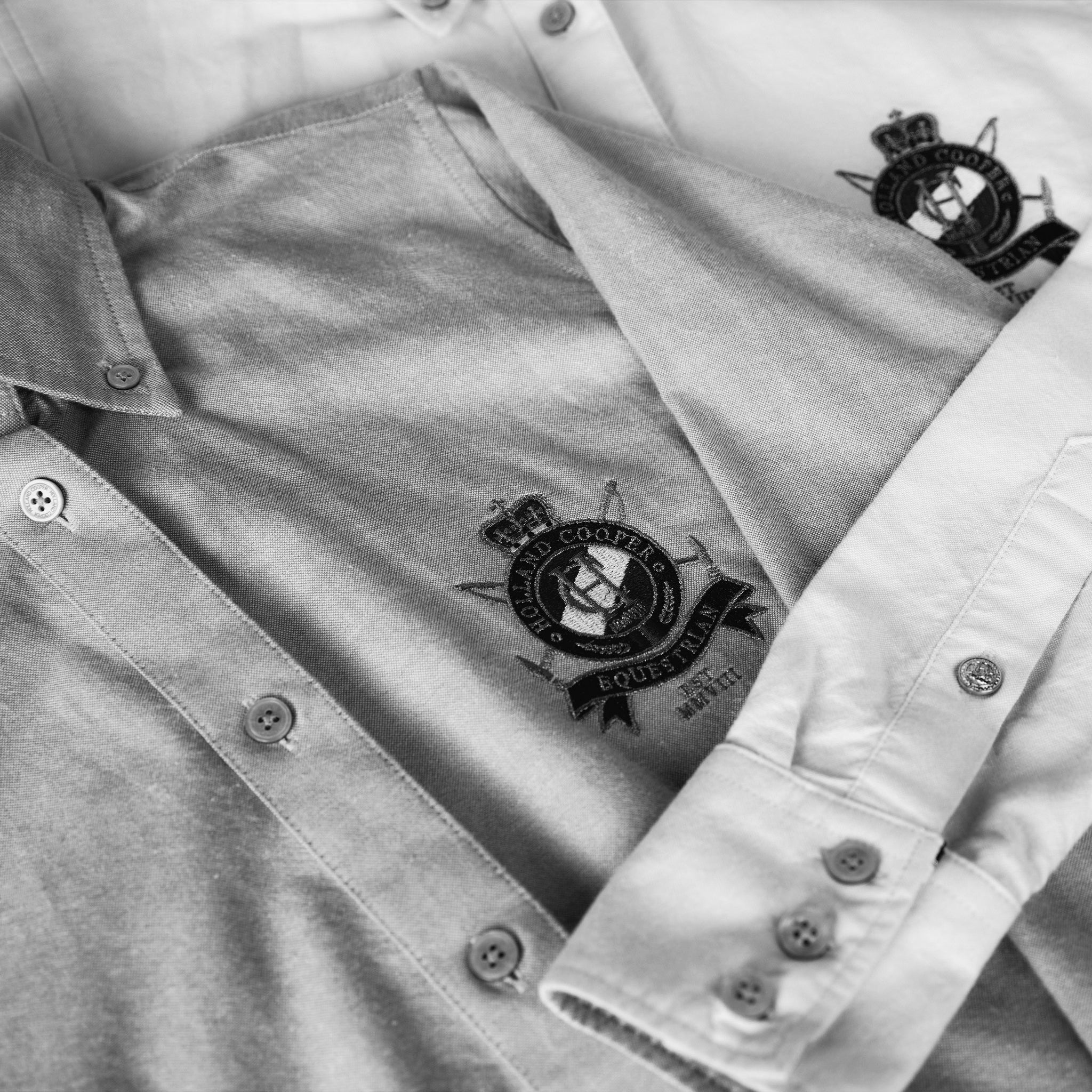 Black and white image of a flat lay of two layered Holland Cooper shirts, focus on HC embroidery
