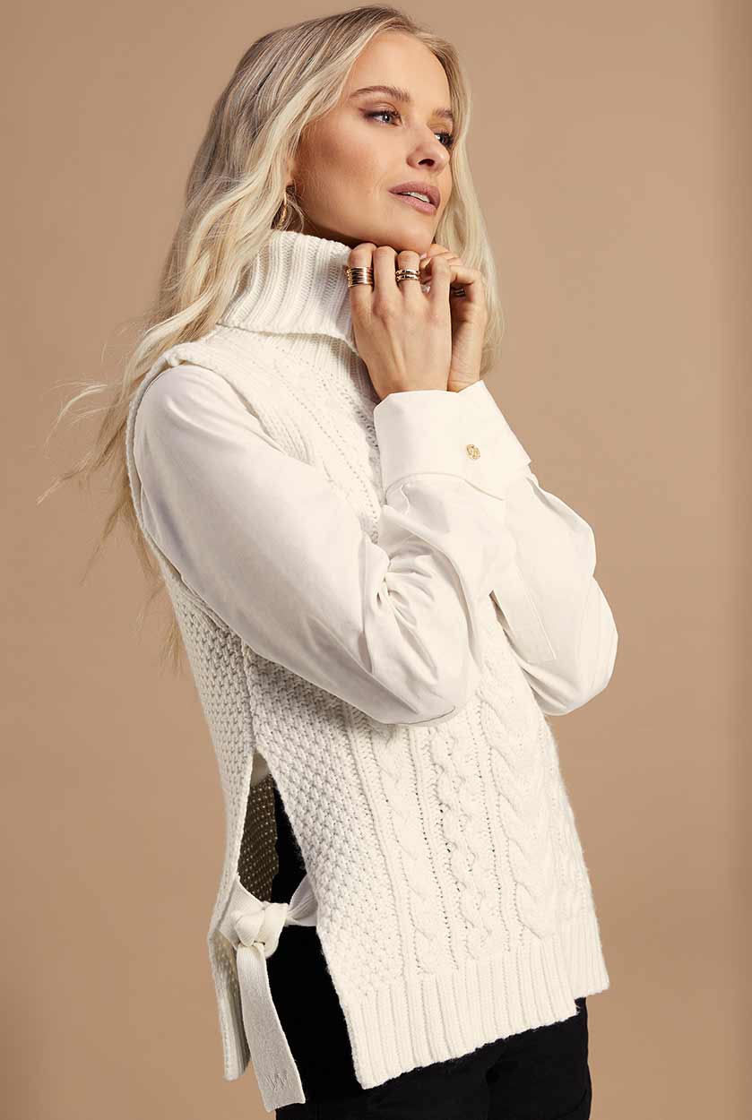Sleeveless white chunky knit cable jumper with a roll neck and ties at each side 