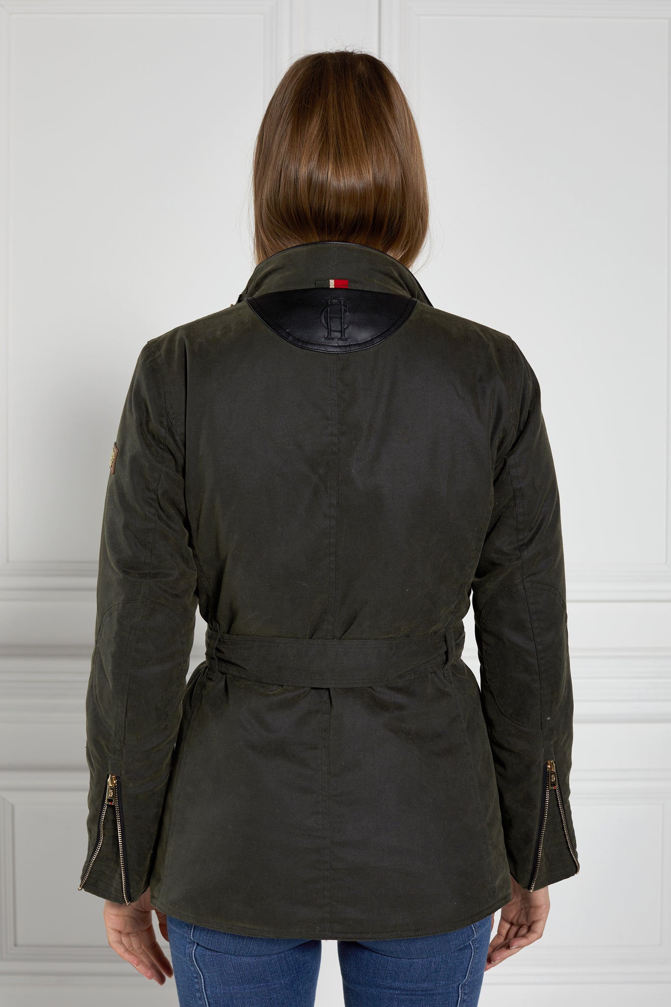back of womens coated wax jacket in dark olive green with four patch pockets belted waist and internal black gilet 
