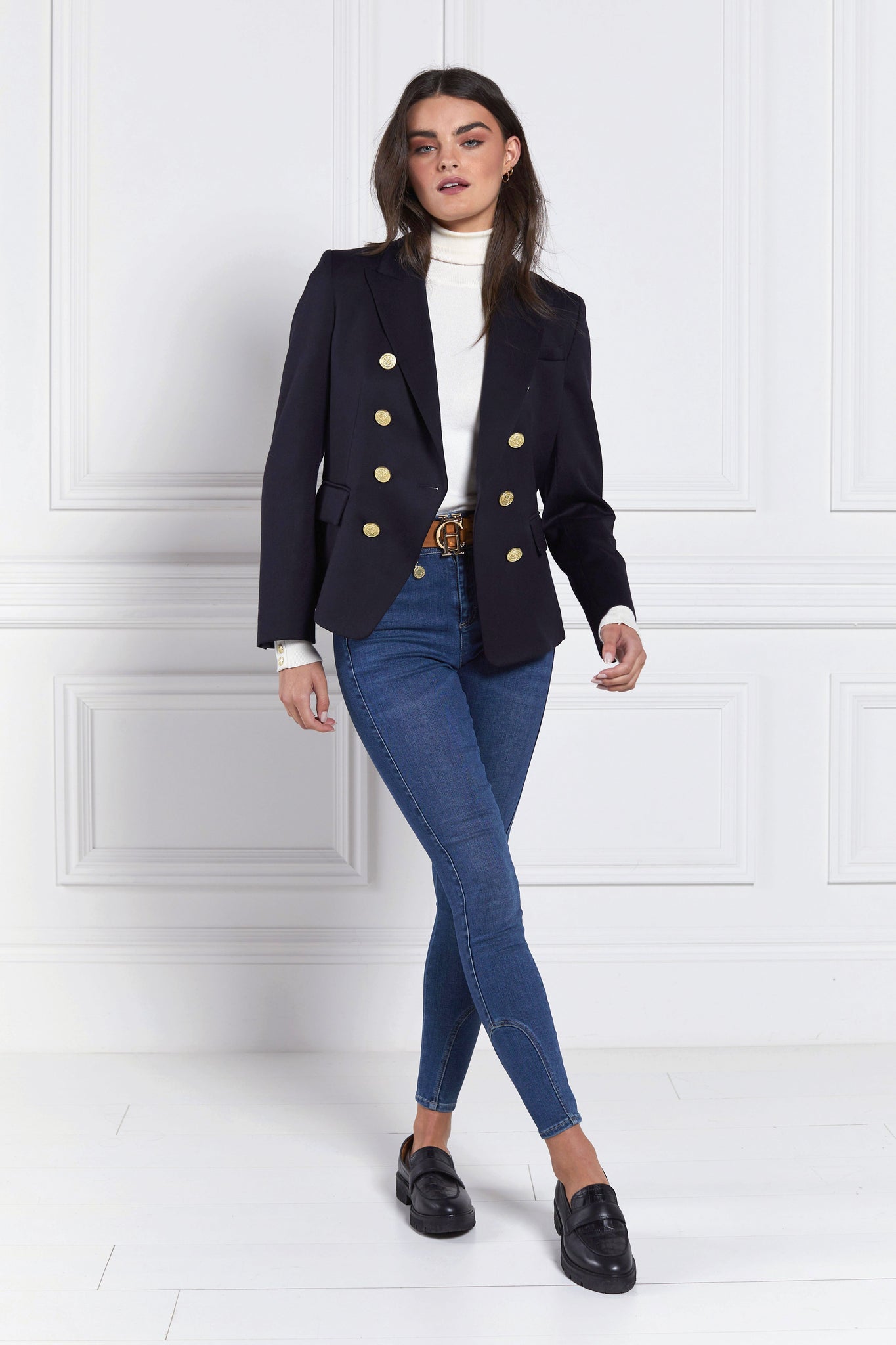 British made double breasted blazer that fastens with a single button hole to create a more form fitting silhouette with two pockets and gold button detailing this blazer is made from navy barathea fabric worn with white roll neck tan belt and classic indigo denim skinny jeans