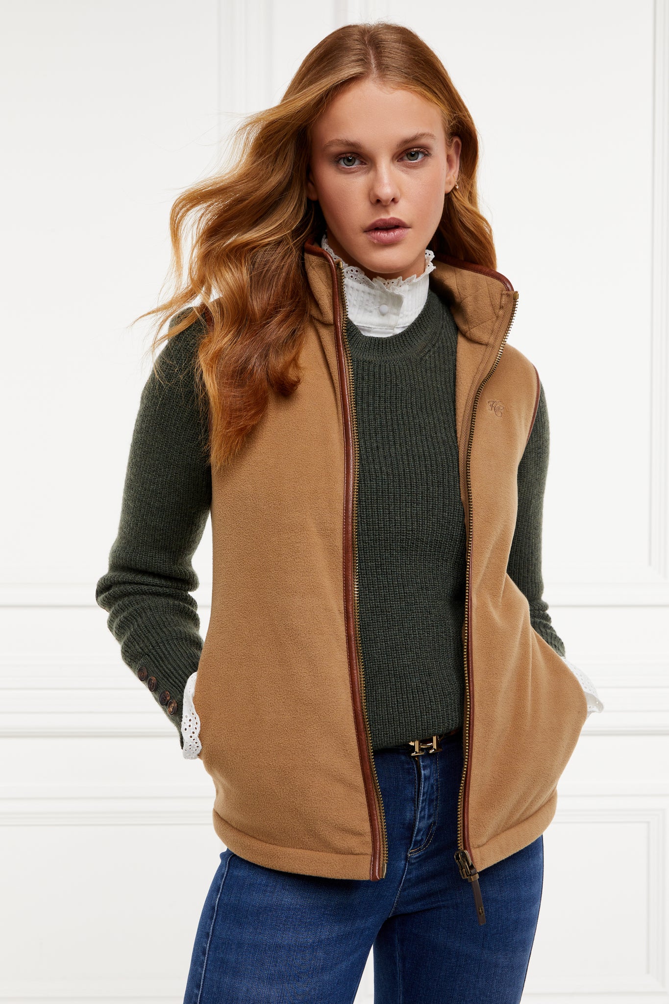 womens fleece gilet in light brown with dark brown leather piping around armholes neckline and down the front zip fastening a dark green knitted sweatshirt a white long sleeve shirt and dark denim skinny jeans