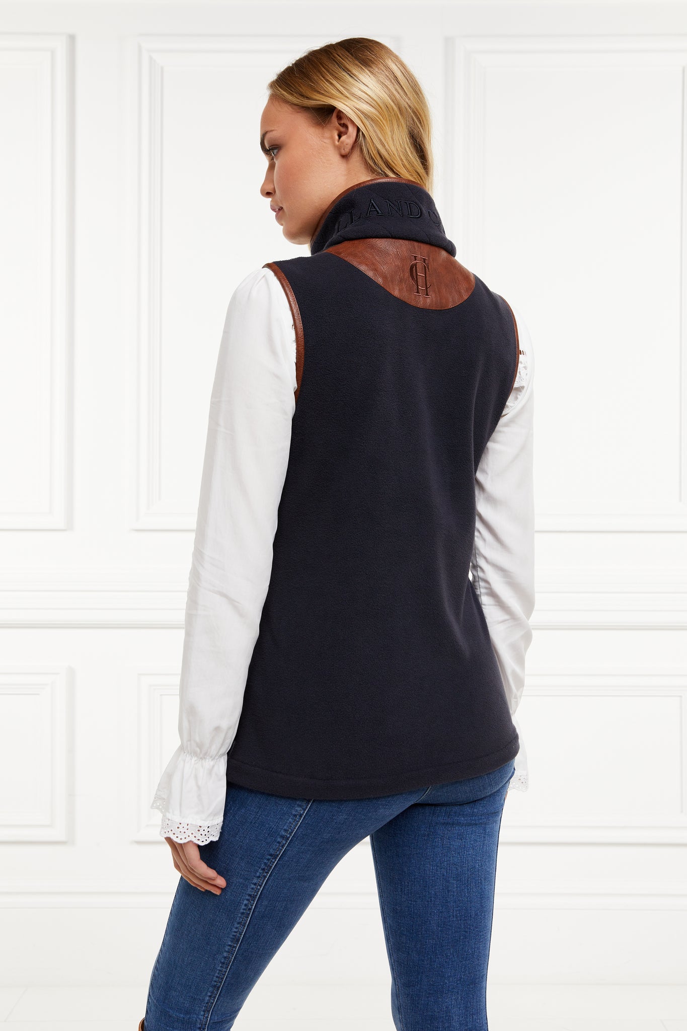 womens fleece gilet in navy with dark brown leather piping around armholes neckline and down the front zip fastening worn with a white shirt and dark denim jeans
