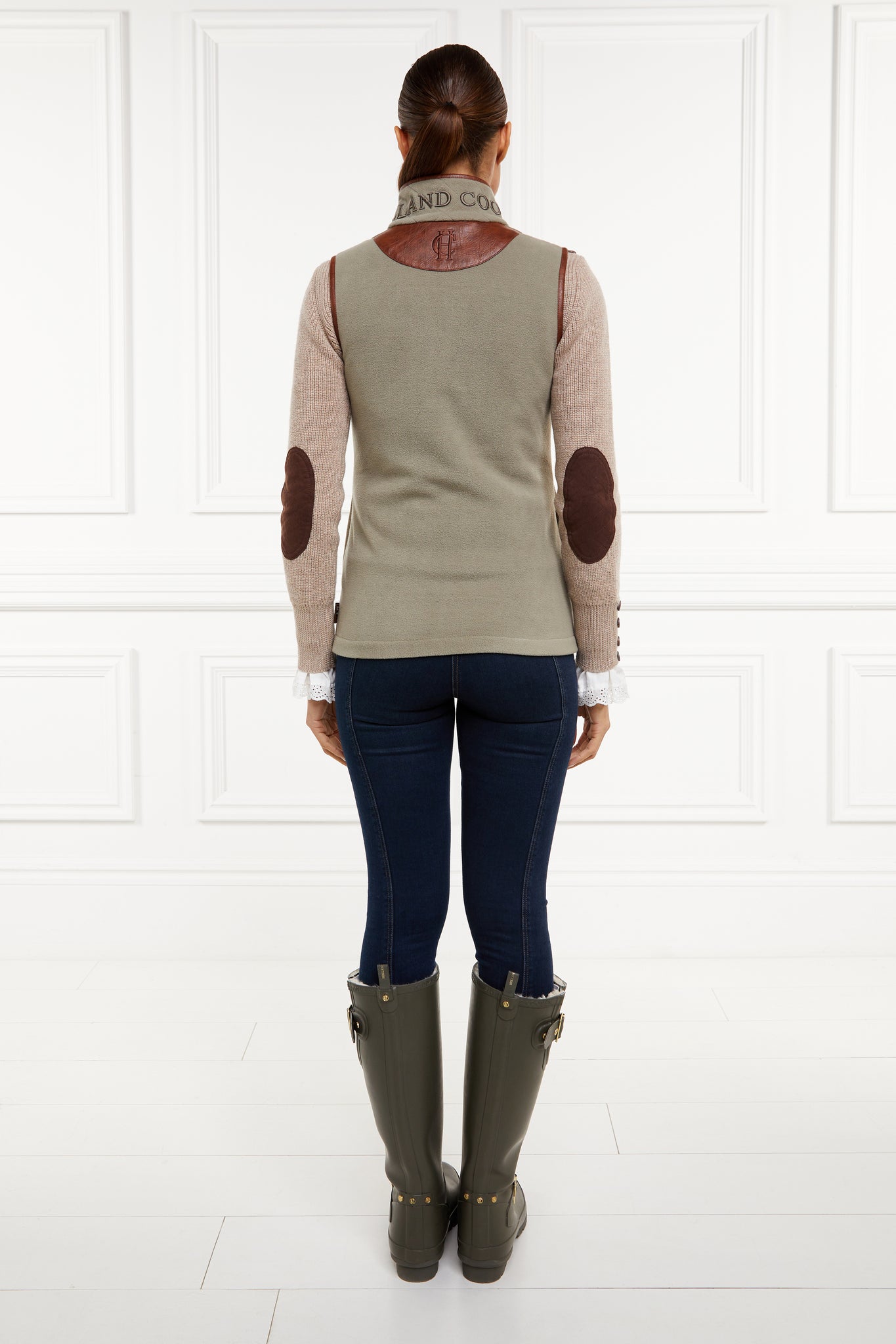womens fleece gilet in sage green with dark brown leather piping around armholes neckline and down the front zip fastening worn with dark green wellingtons indigo skinny jeans and a beige knitted jumper