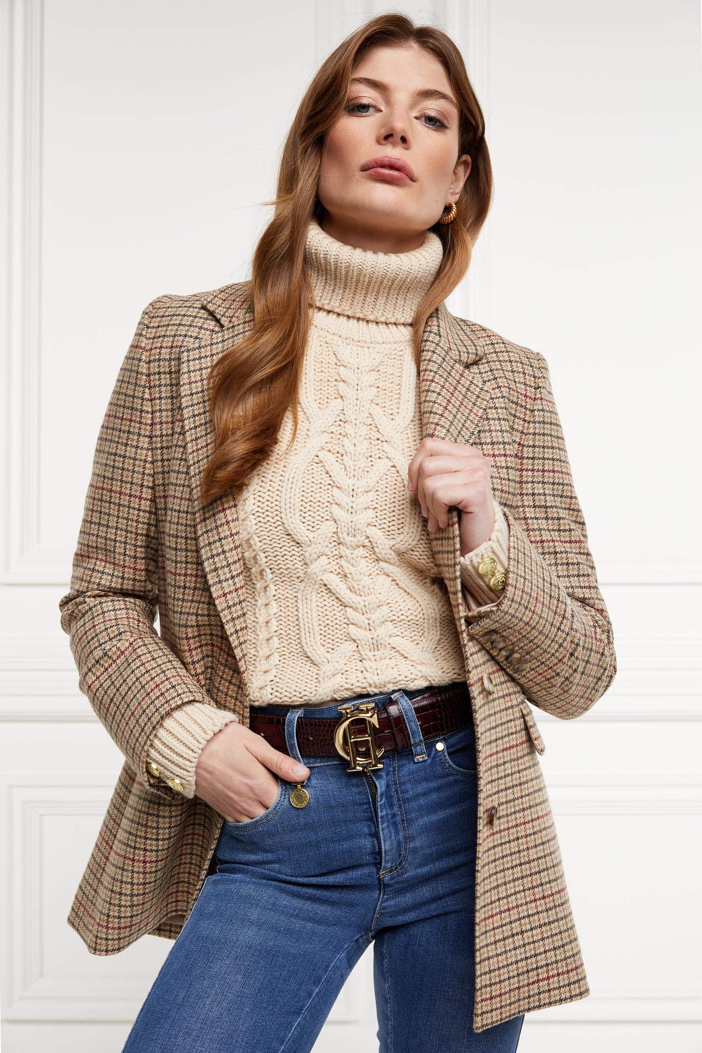 a chunky cable knit roll neck jumper in oatmeal with dropped shoulders and thick ribbed cable trims and gold buttons on cuffs and collar worn with a single breasted blazer is charlton tweed
