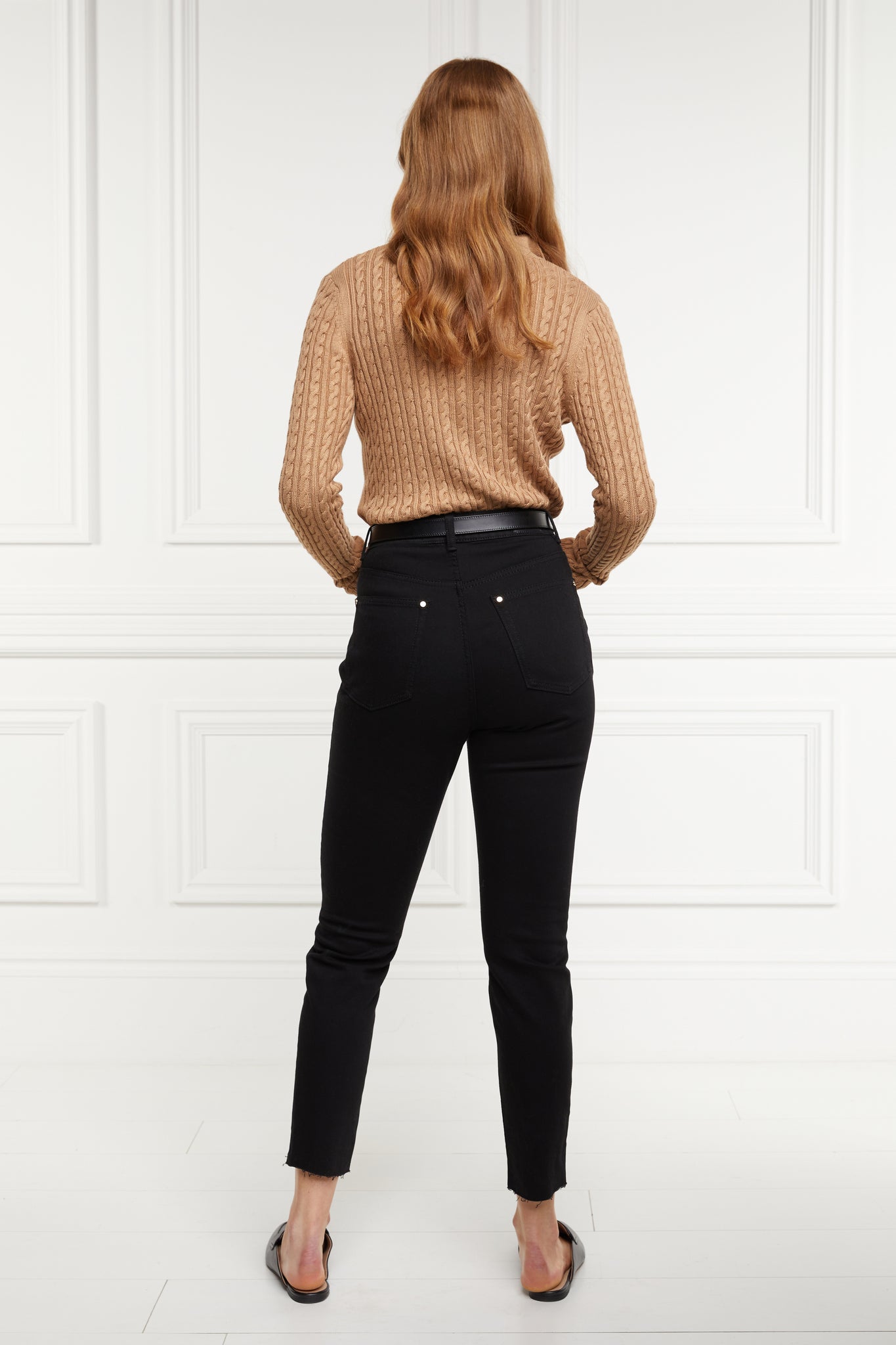 back of womens high rise black denim slim fit jean with raw hem and two open pockets on the front and back with gold stirrup charm to the belt loop