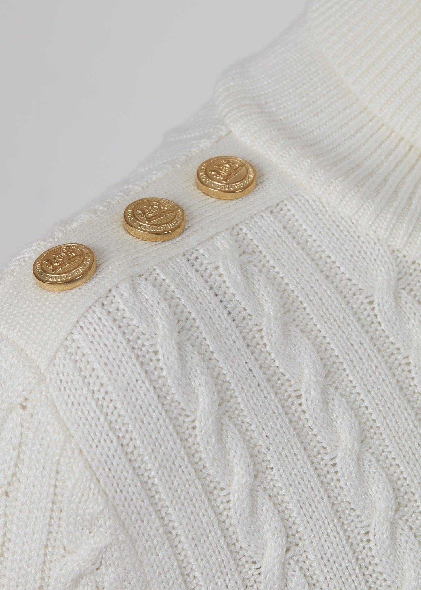 gold button detail across shoulder of womens cable knit jumper in white with ribbed roll neck cuffs and hem
