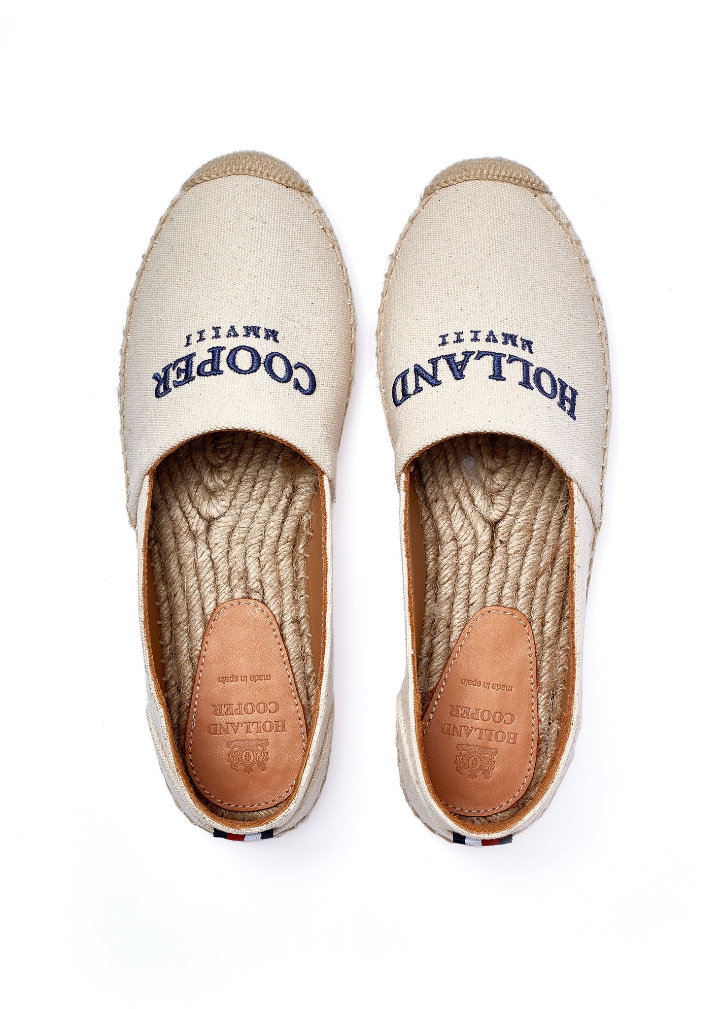 Birds eye view of classic style natural canvas espadrille with plaited jute sole and jute toe cap with navy embroidered branding on top and a red, white and blue small tag on the heel
