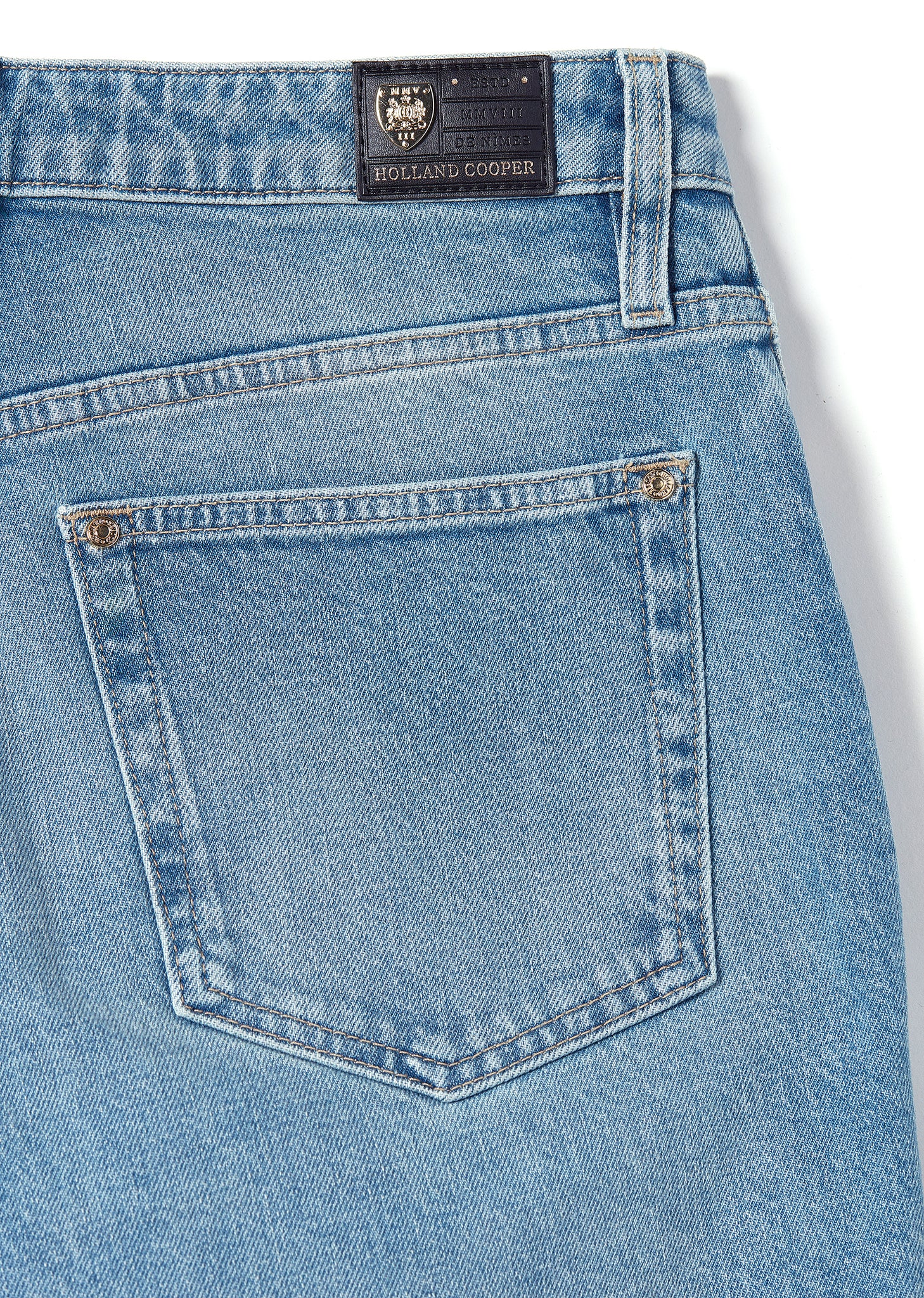 back pocket detail on womens high rise blue denim slim fit jean with raw hem and two open pockets on the front and back with gold stirrup charm to the belt loop