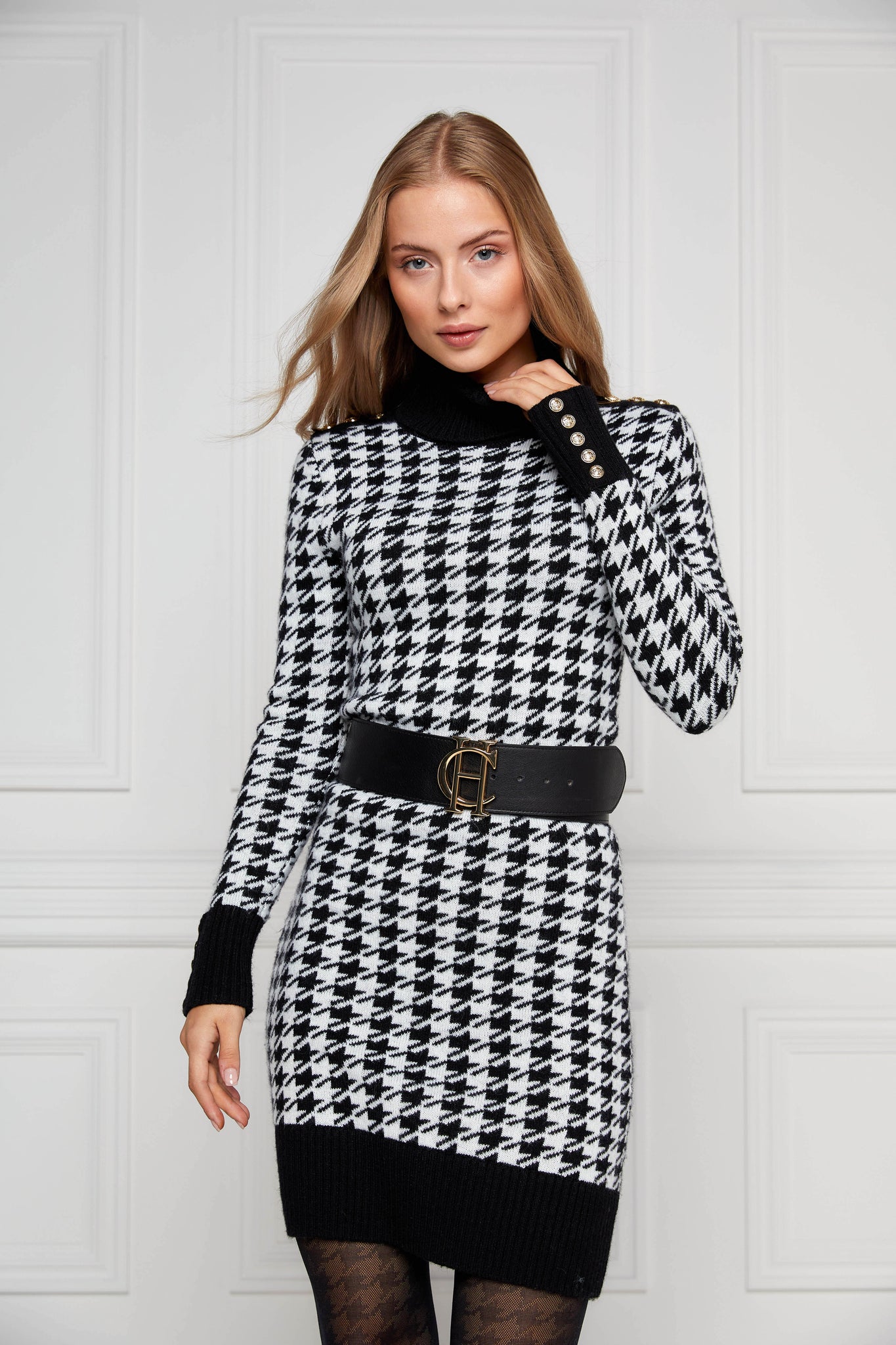 womens black and white houndstooth roll neck jumper dress with contrast black cuffs and ribbed hem with gold button detail on the cuffs and shoulders worn with wide black belt
