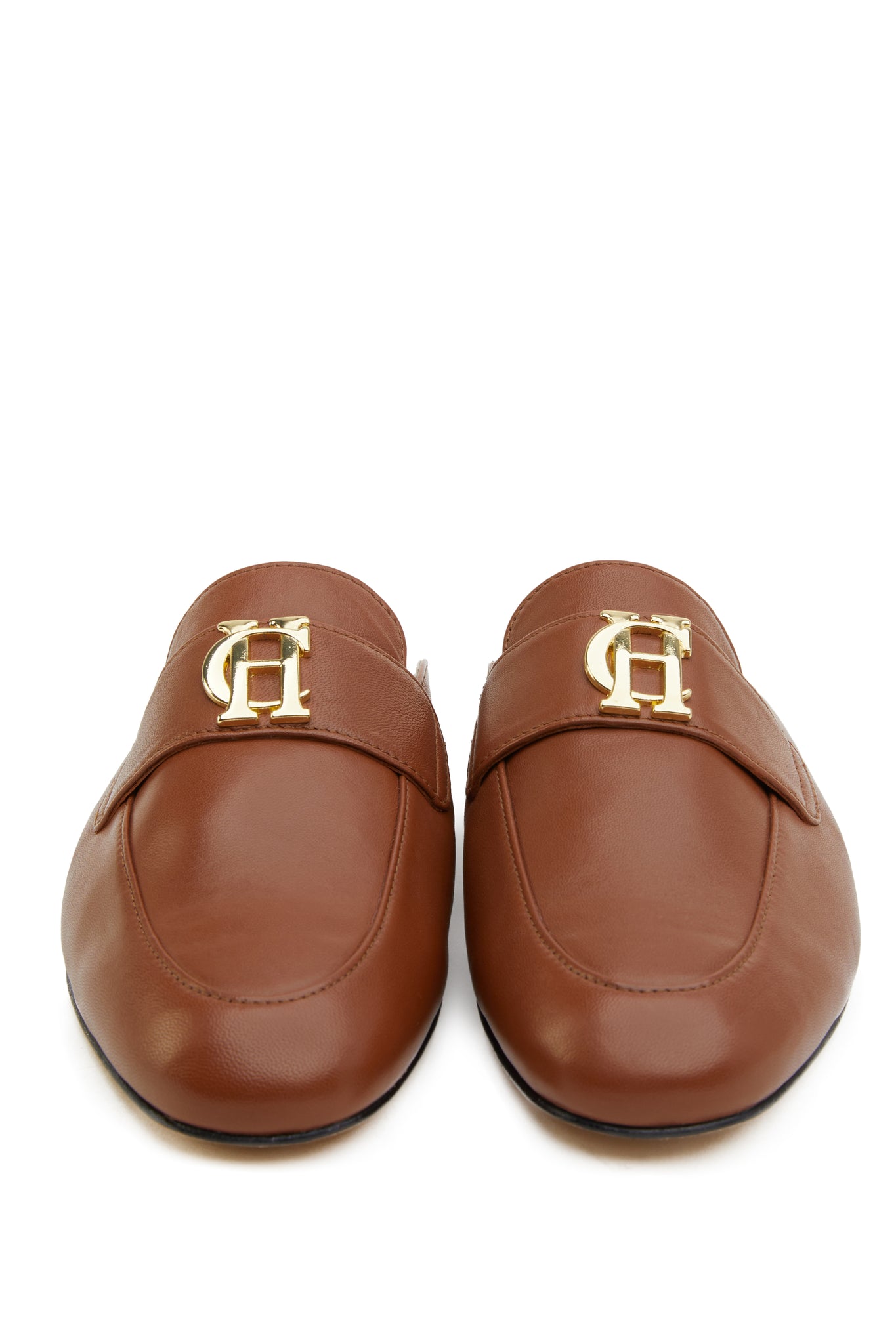 Front shot of tan leather backless loafers with a slightly pointed toe and gold hardware to the top