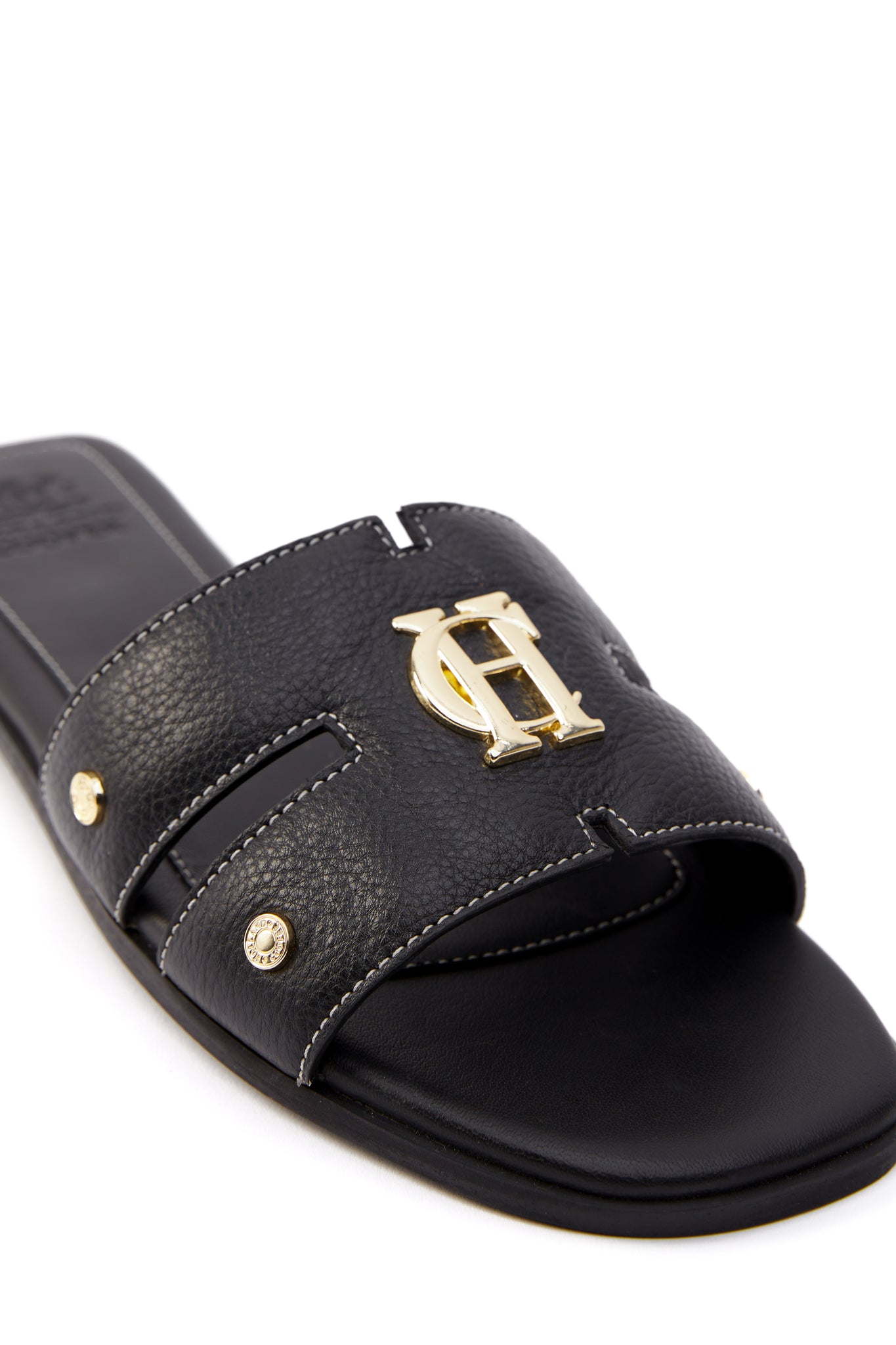 Close up of black leather sliders with contrast white stitching, a black leather sole and gold hardware