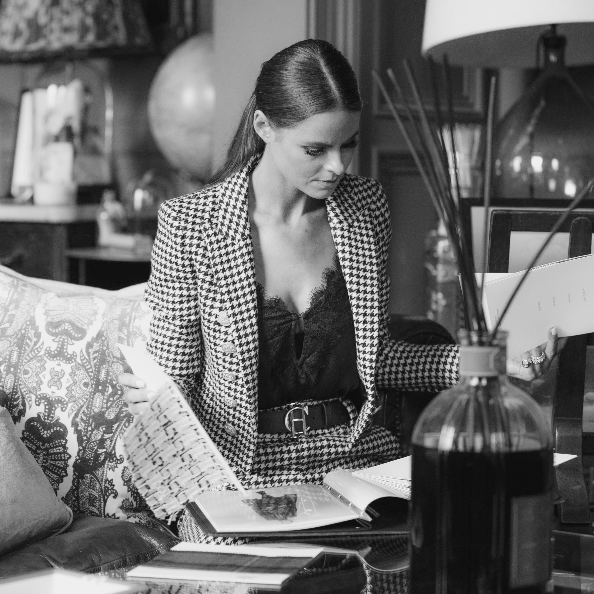 Black and white image of Jade Holland Cooper, owner of Holland Cooper, sat looking at magazines dressed in black and white houndstooth womens blazer and trousers