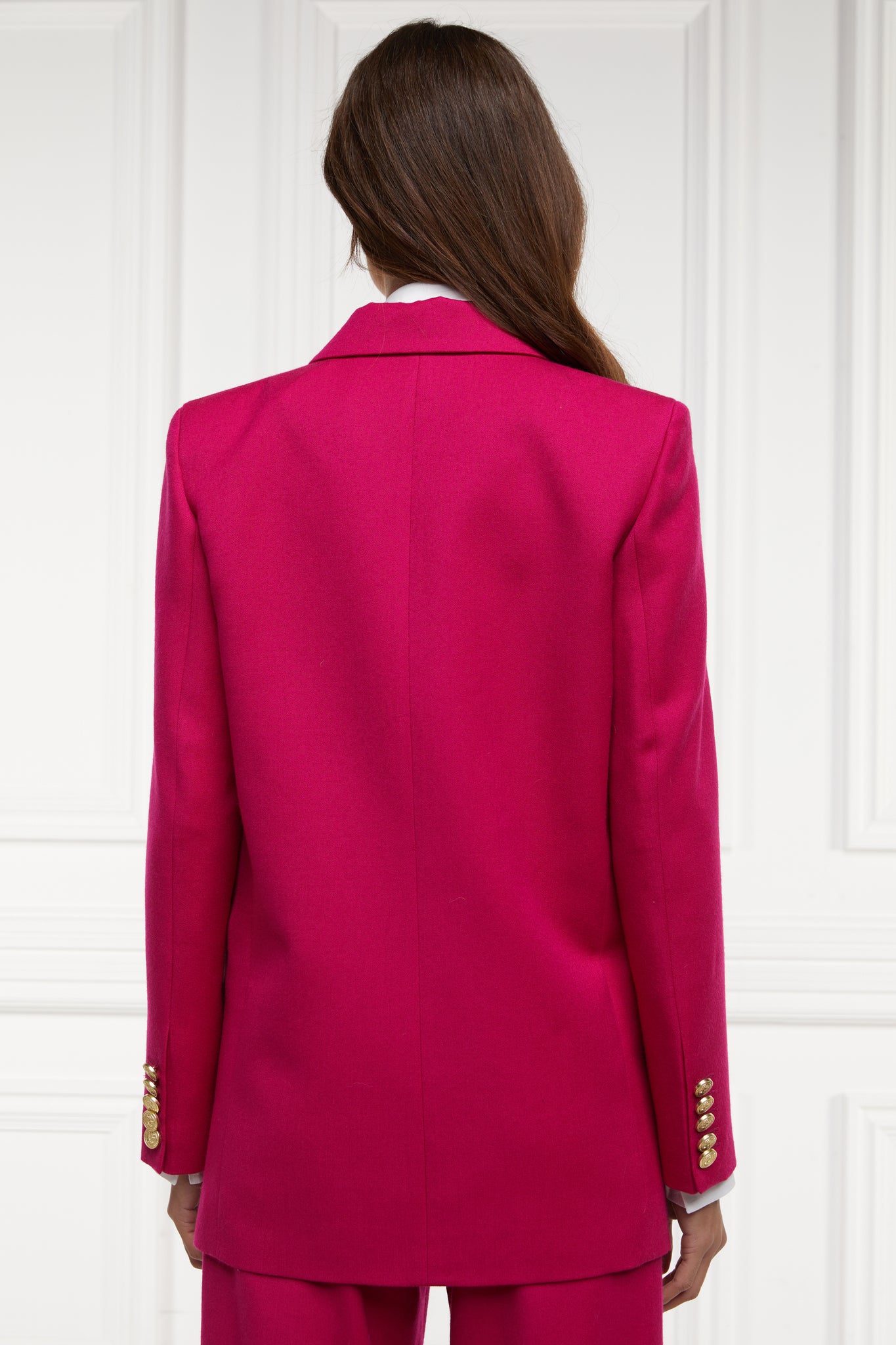 back of longline double breasted wool blazer in hot pink tailor made in britain with relaxed fit welt pockets and gold buttons on the front and cuffs