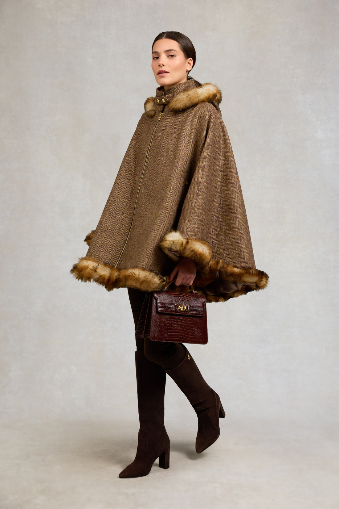 Brown herringbone cape with shearling trim, worn with tall brown boots and a handheld bag