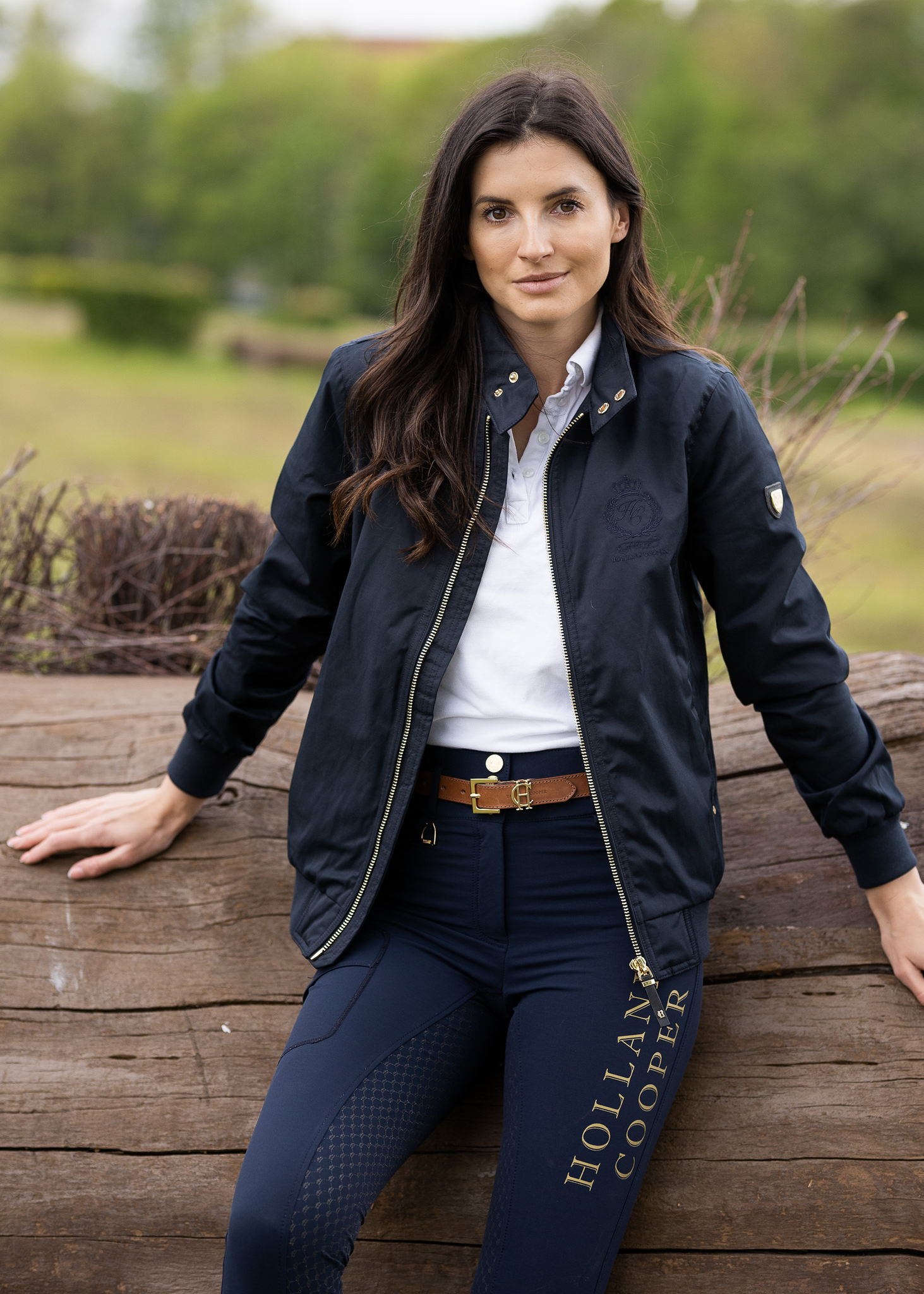 Womens navy 100% waterproof hoodless bomber style jacket with ribbed cuffs and hem, two pockets on hips a full zip down the centre front worn with white polo shirt and navy breeches