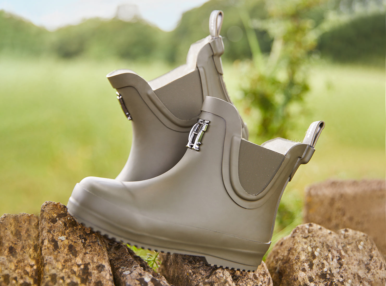 Children's wellingtons in green sat on cotswold stone wall with a green grass background