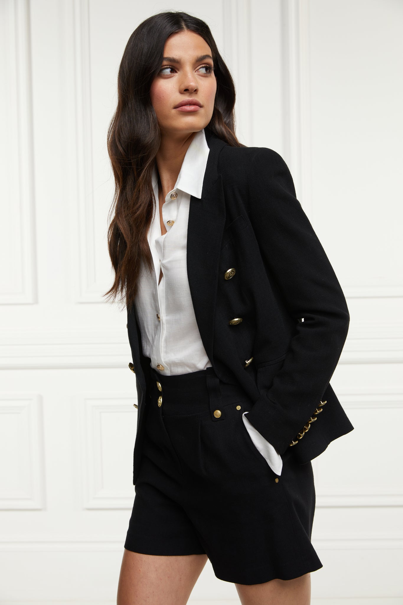 womens black linen tailored shorts with two single knife pleats and centre front zip fly fastening with two gold stud buttons worn with white classic shirt and black double breasted black linen blazer