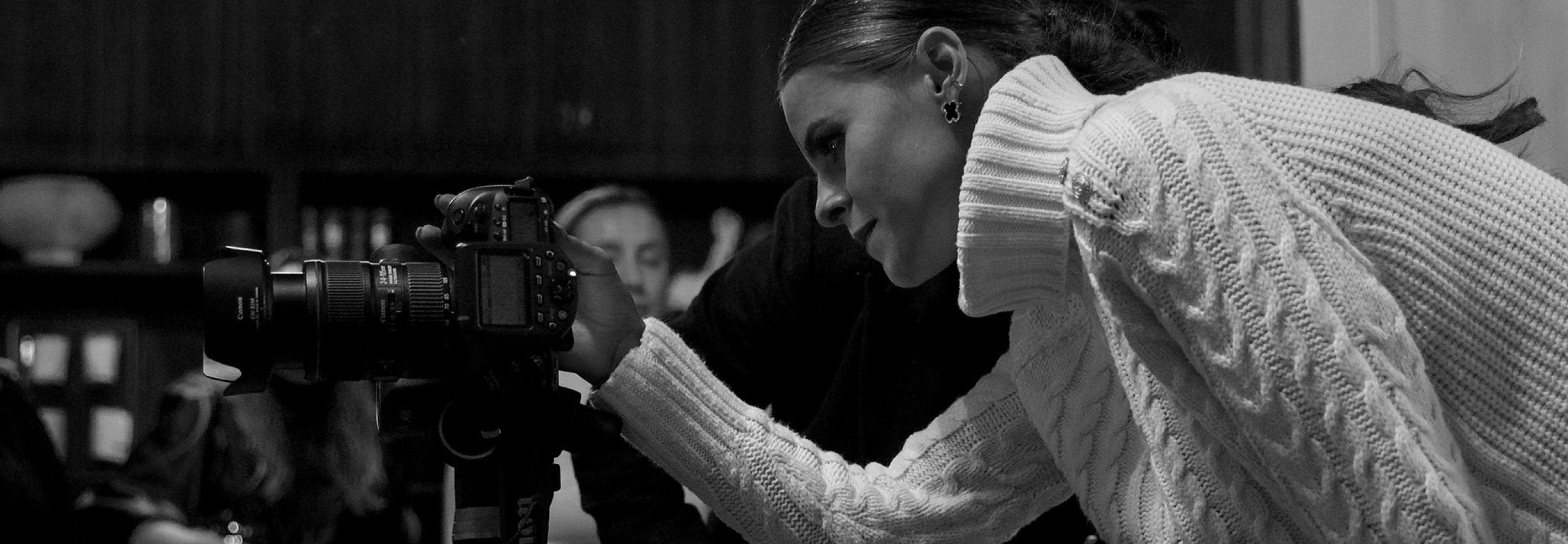 Black and white image of Jade Holland Cooper in white roll neck jumper looking into back of DSLR camera