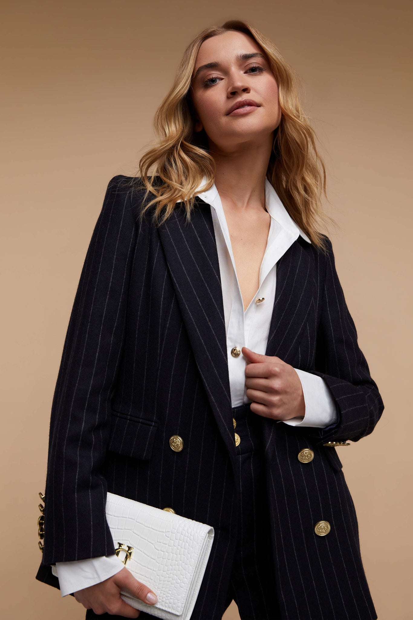 double breasted wool blazer in navy and cream chalk pinstripe with two hip pockets and gold button detials down front and on cuffs and handmade in the uk worn with classic white shirt tailored trousers in matching pinstripe and white clutch bag