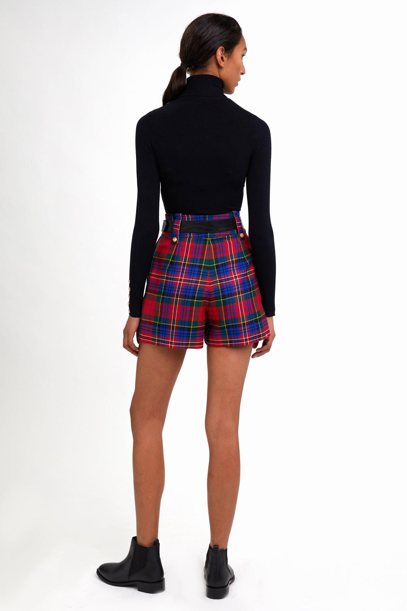 back of womens red blue and green tartan high rise tailored shorts with two single knife pleats and centre front zip fly fastening with twin branded gold stud buttons and side hip pockets with branded rivet detailing at top and bottom of pockets worn with black roll neck