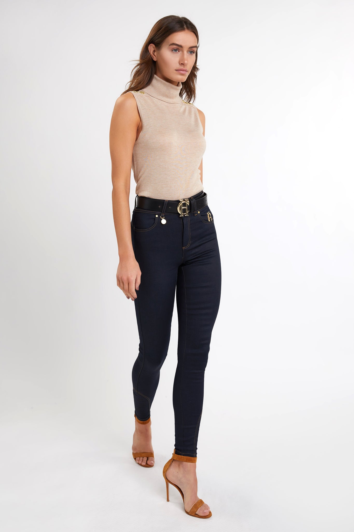 fitted lightweight sleeveless rollneck knit in camel with gold button detail across shoulders worn with navy skinny jeans and black belt