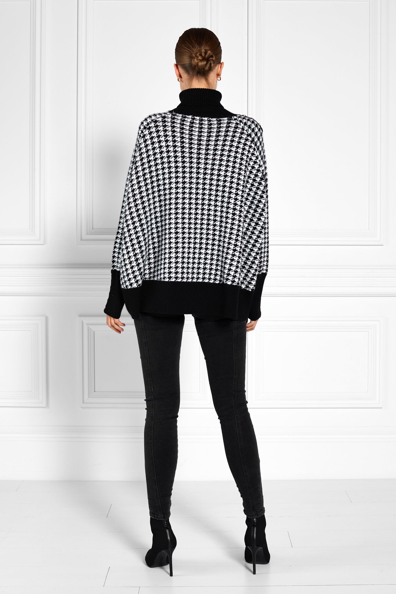 back of womens funnel neck batwing shaped cape in a white and black houndstooth knit with split side detail and contrast black neckline cuffs and hem