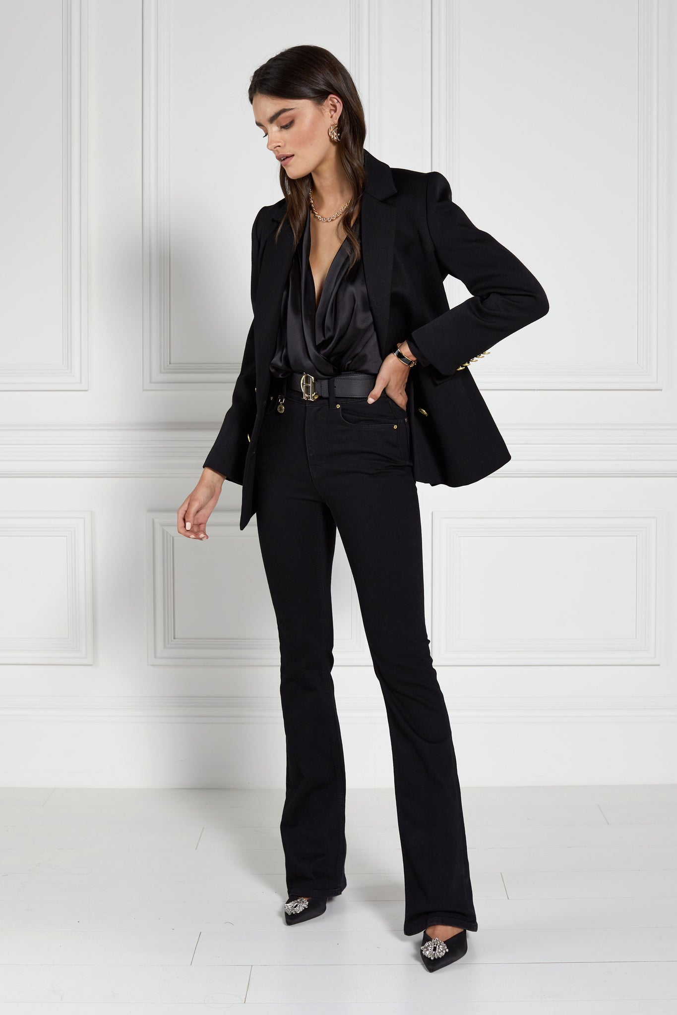 double breasted wool blazer in black with two hip pockets and gold button details down front and on cuffs and handmade in the uk worn with black silk shirt and black flared jeans 