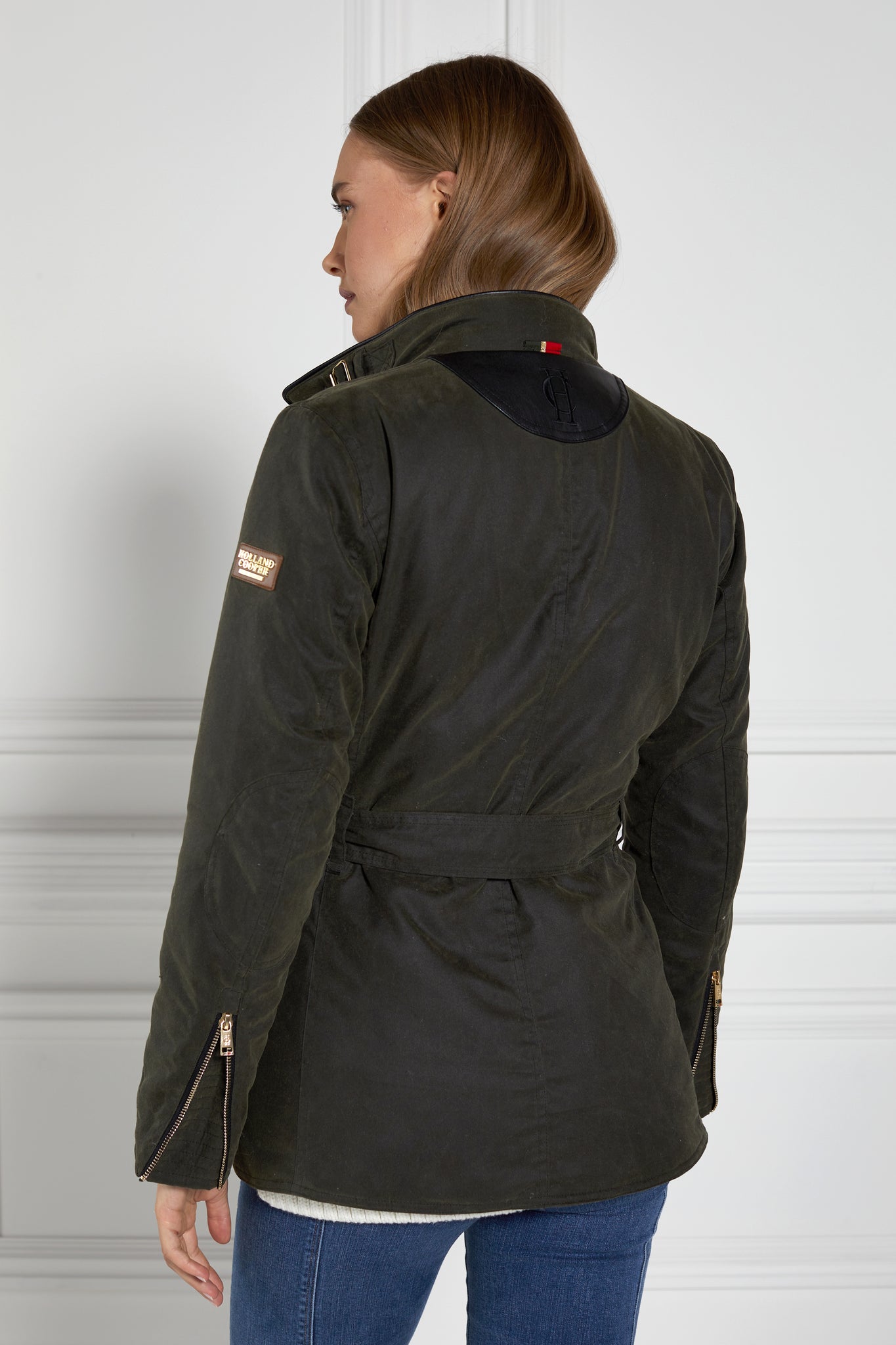 back of womens coated wax jacket in dark olive green with four patch pockets belted waist and internal black gilet 