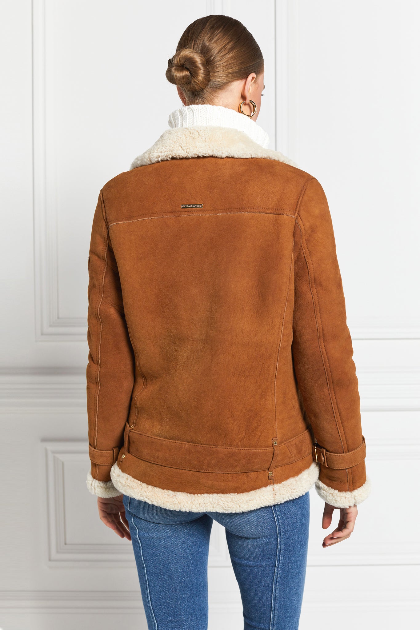 back of classic aviator jacket in tan leather with cream shearling inside that accents the cuffs hem and collar with belt detail on the hem and cuffs three pockets and angular zip fastening