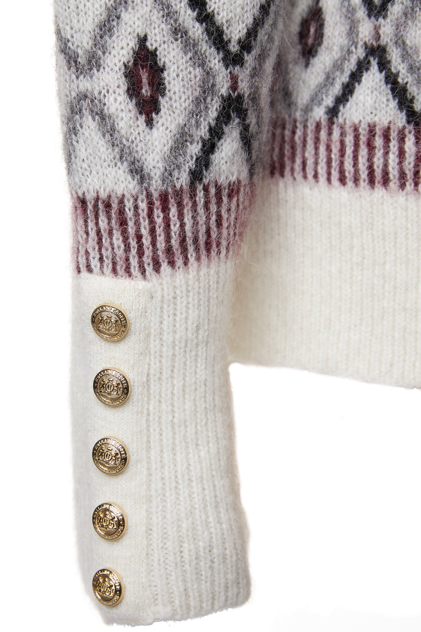 gold button detail on cuffs of a classic cream roll neck jumper with fairisle knit in red and grey around the shoulders waistline and cuffs and a split ribbed hem 