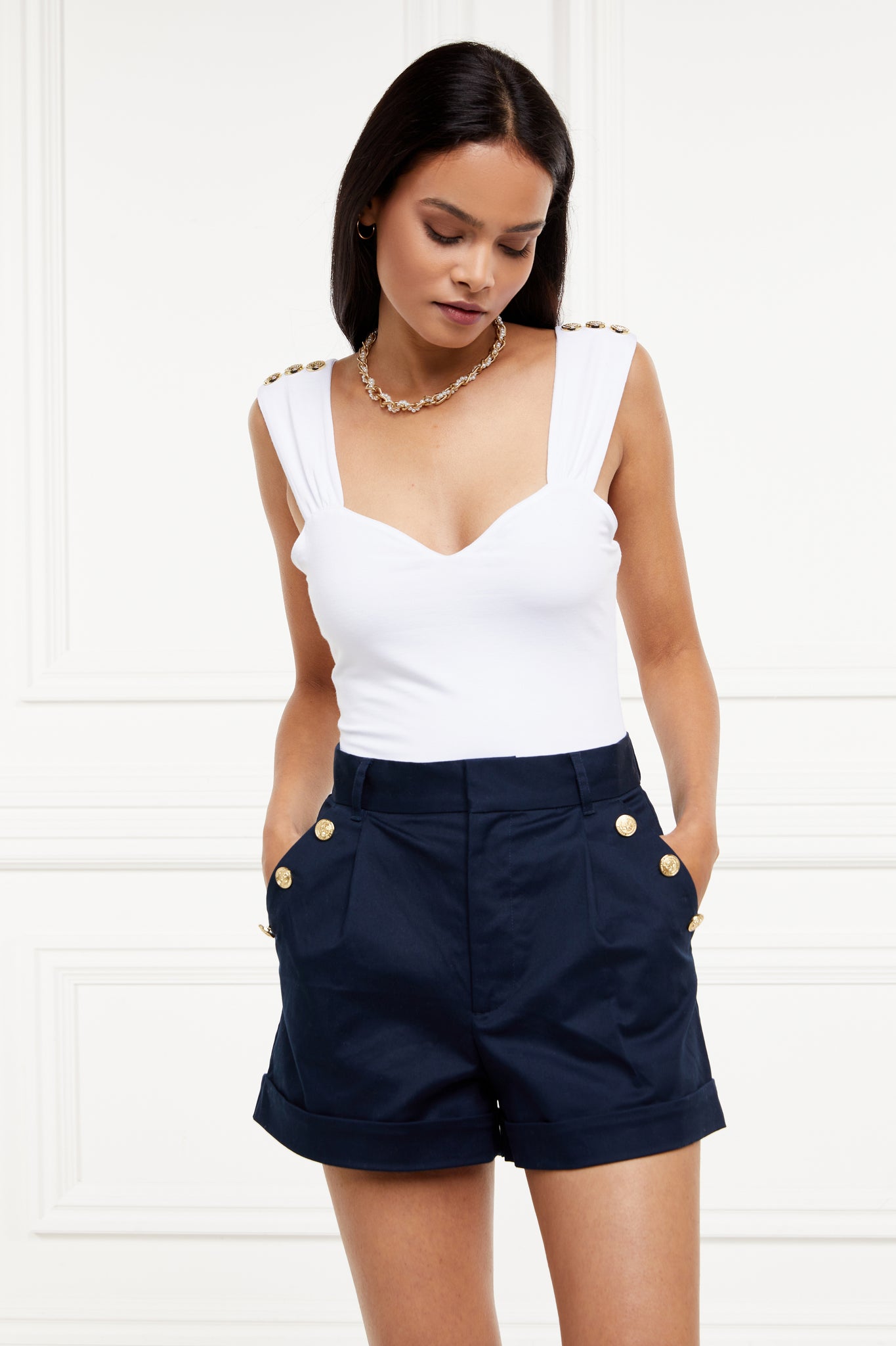 womens navy high rise tailored shorts with decorative gold rivets that follow the pocket line in a sailor style with a turned up hem worn with white bodysuit