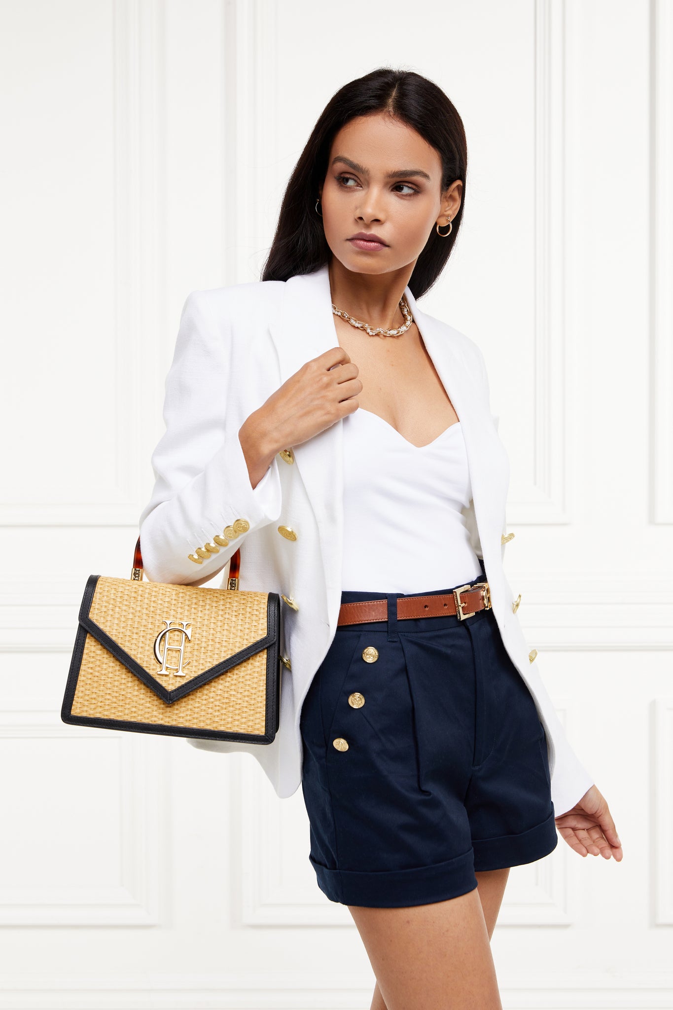 womens navy high rise tailored shorts with decorative gold rivets that follow the pocket line in a sailor style with a turned up hem worn with white bodysuit and white double breasted blazer