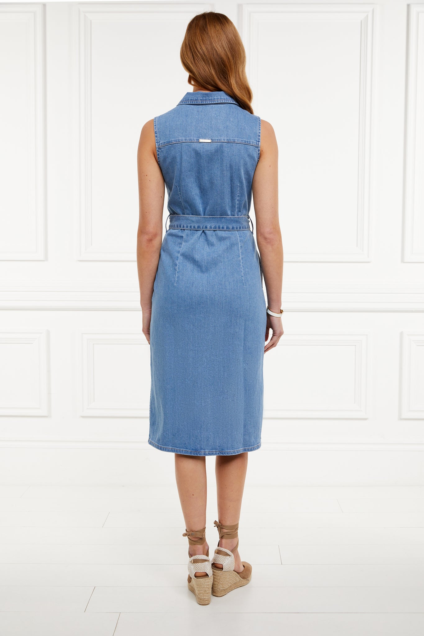 back shot of womens blue denim sleeveless midi dress with tie around the waist and gold buttons down the front