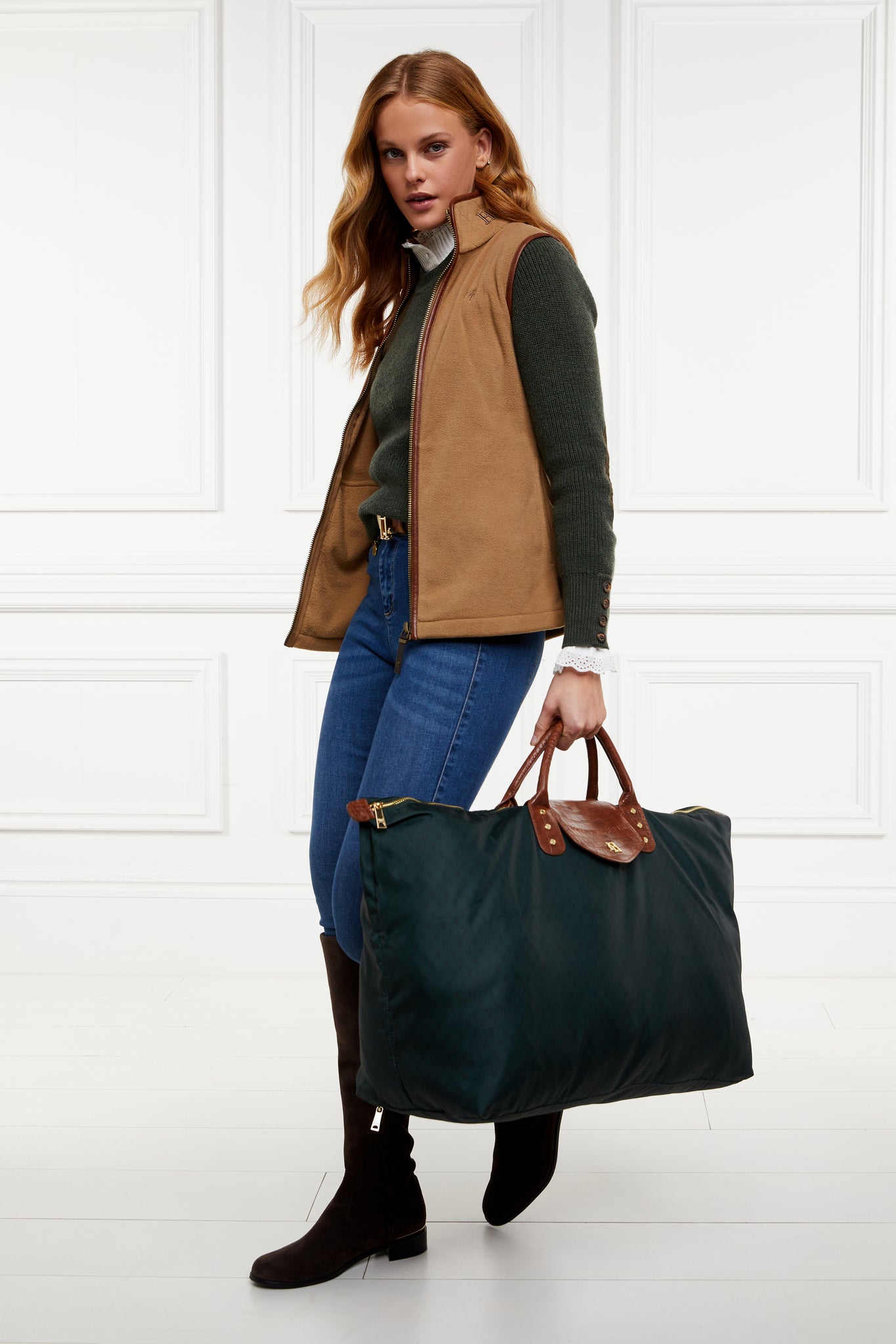 womens fleece gilet in light brown with dark brown leather piping around armholes neckline and down the front zip fastening a dark green knitted sweatshirt a white long sleeve shirt dark denim skinny jeans a dark green holdall and black suede knee high boots