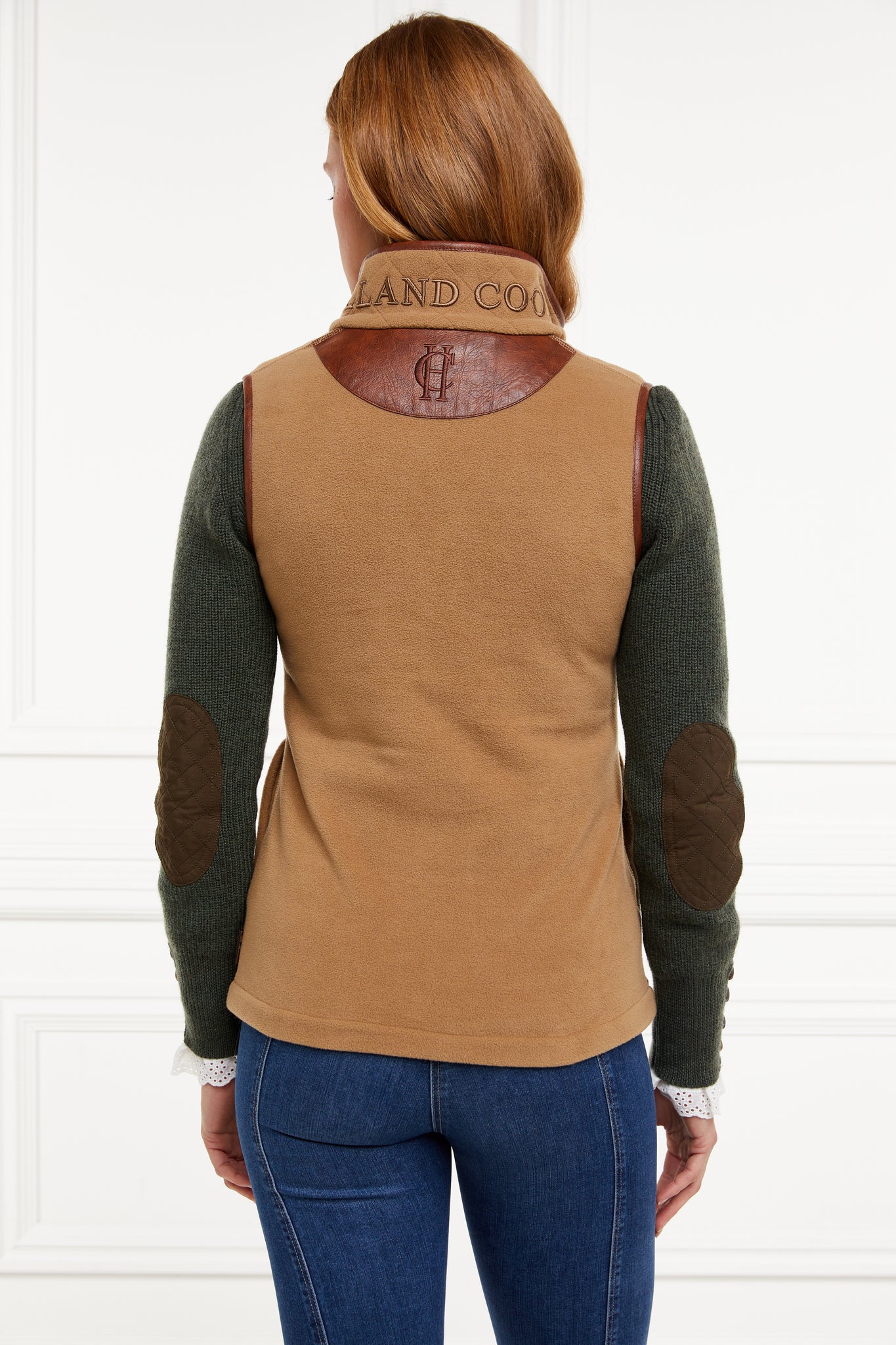 womens fleece gilet in light brown with dark brown leather piping around armholes neckline and down the front zip fastening worn with a dark green knitted sweatshirt and dark denim jeans