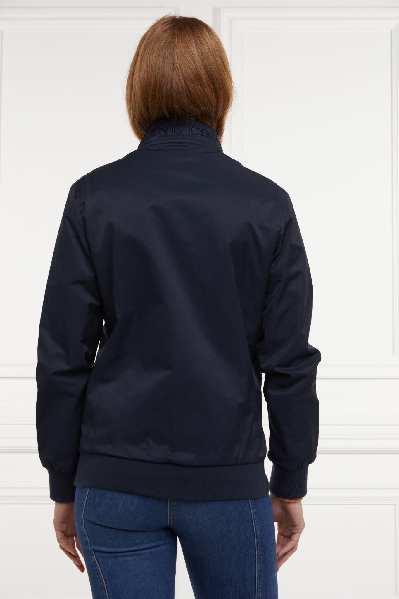 Back of Womens navy 100% waterproof hoodless bomber style jacket with ribbed cuffs and hem, two pockets on hips a full zip down the centre front 