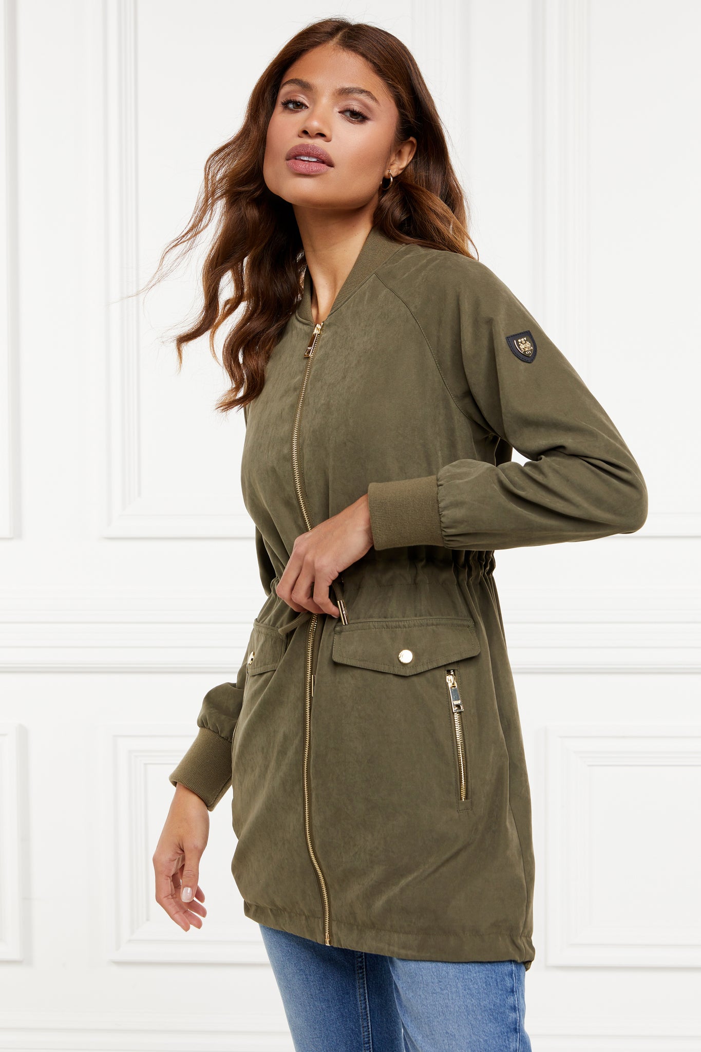 brushed suede longline lightweight parka jacket in khaki with an adjustable drawstring waist and fishtail hem and ribbed baseball style jersey collar and cuffs finished with gold hardware and gold shield on sleeve