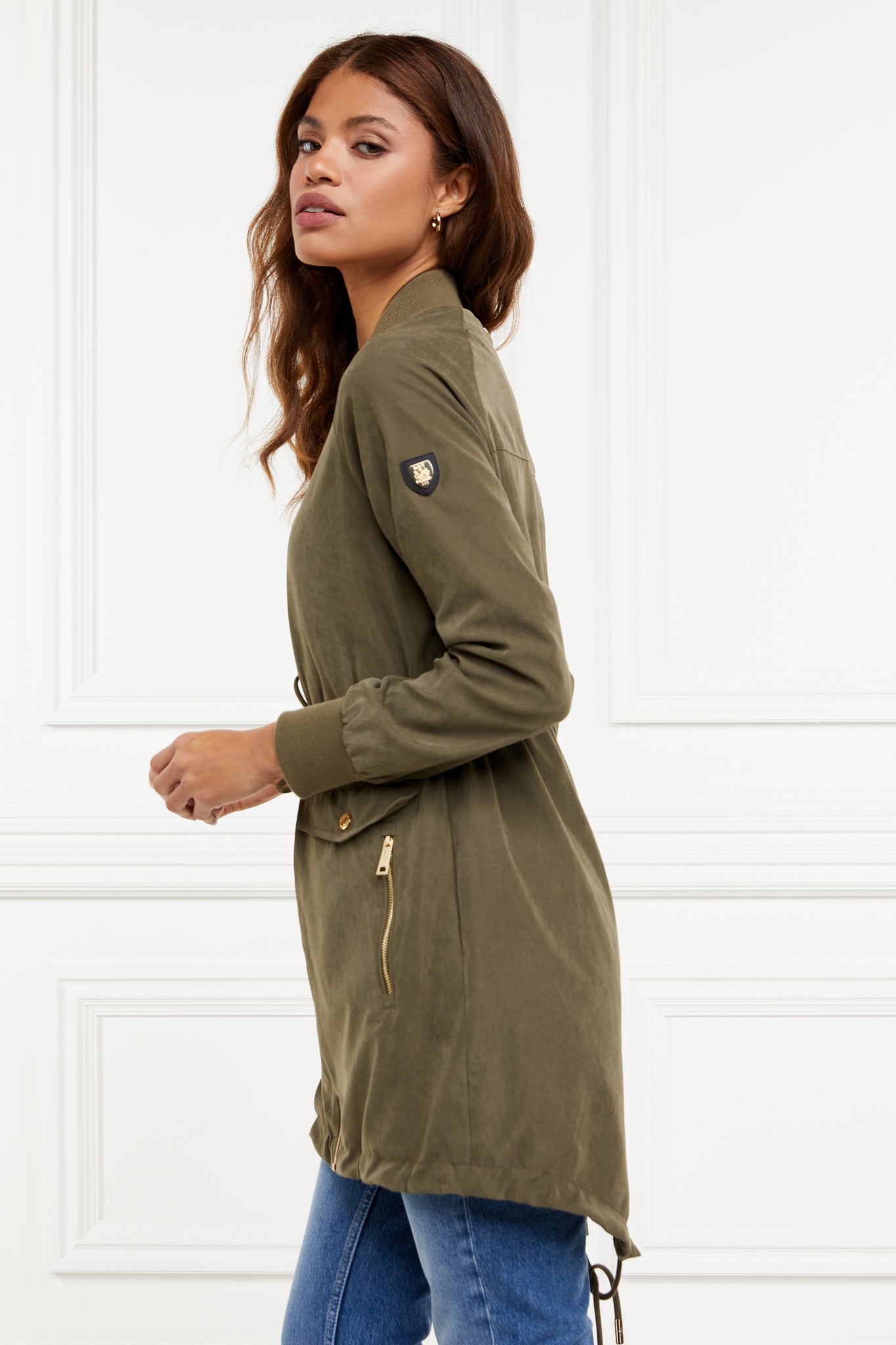 side of brushed suede longline lightweight parka jacket in khaki with an adjustable drawstring waist and fishtail hem and ribbed baseball style jersey collar and cuffs finished with gold hardware and gold shield on sleeve