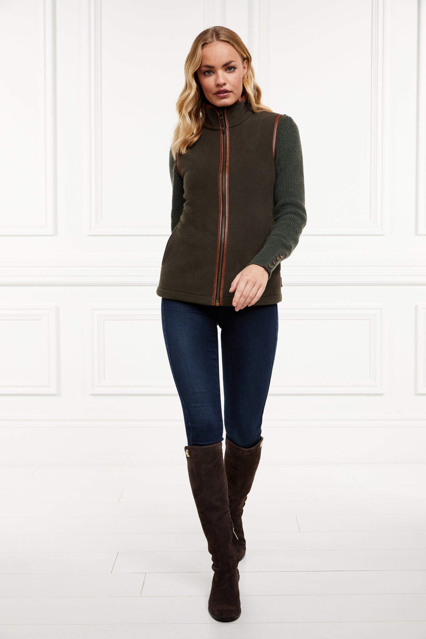 womens fleece gilet in khaki with tan leather piping around armholes neckline and down the front zip fastening worn with indigo skinny jeans and knee high suede boots in chocolate 