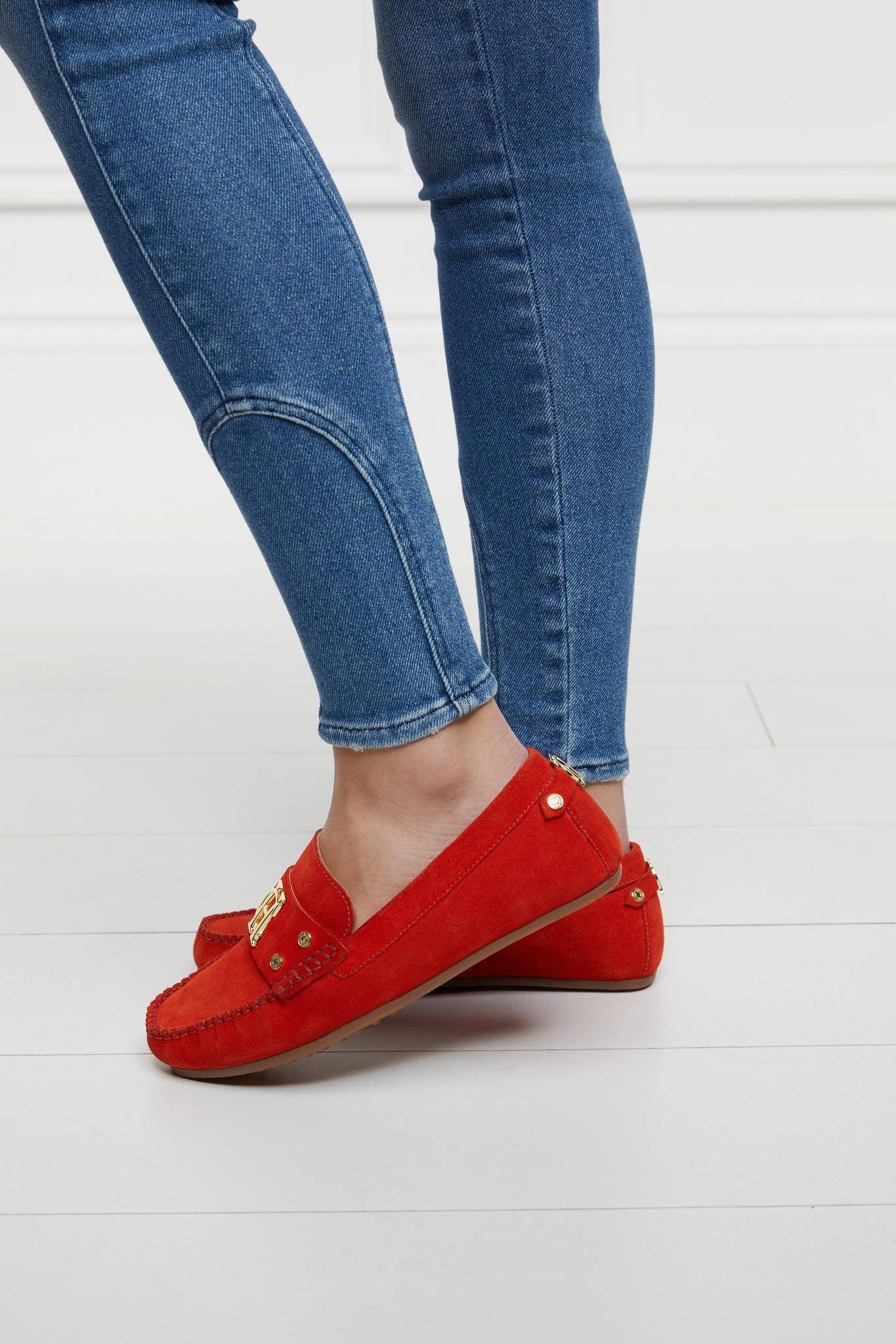 side view of orange suede loafers with a leather sole and top stitching details and gold hardware paired with denim jeans