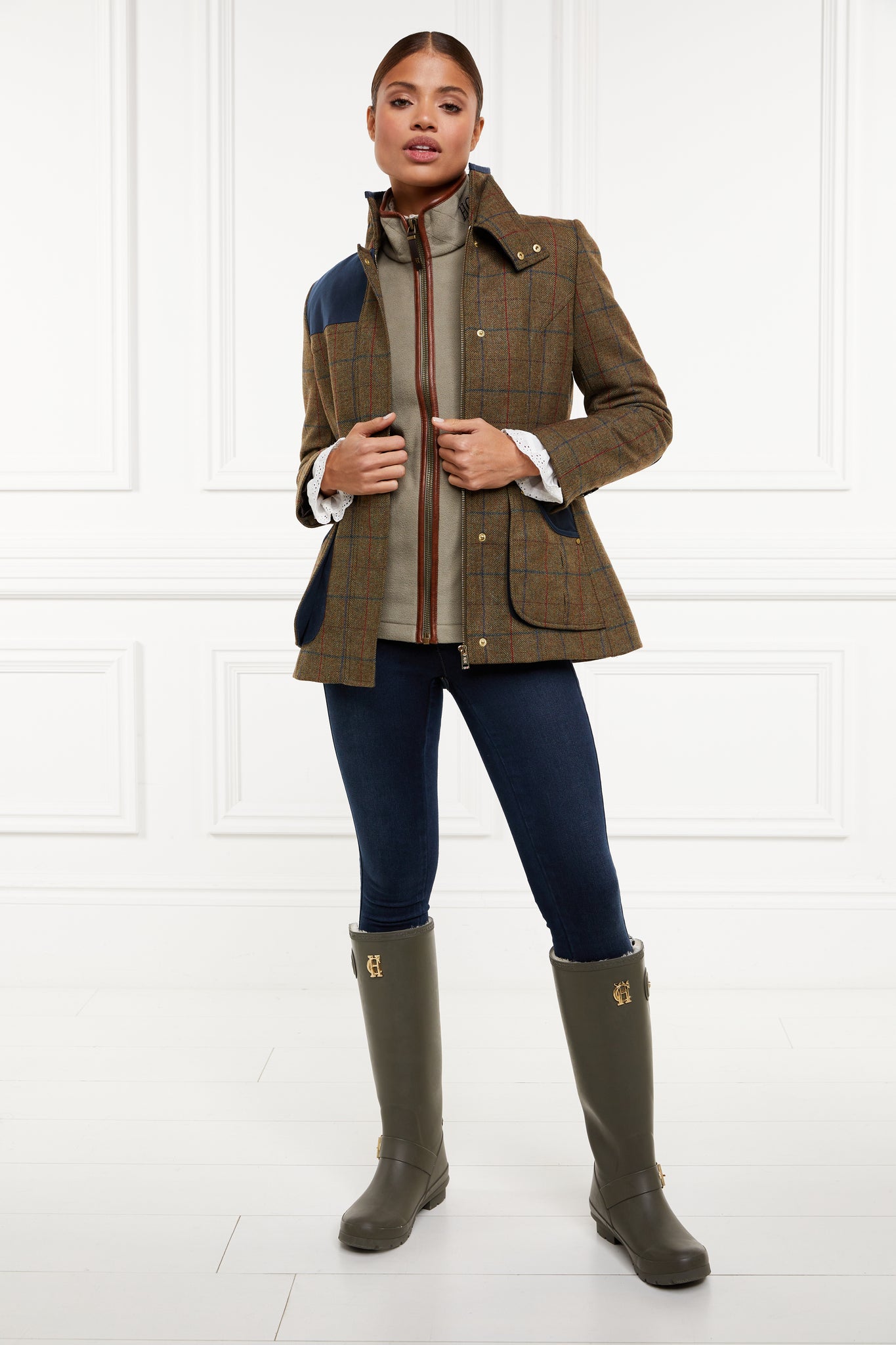 womens fleece gilet in sage green with dark brown leather piping around armholes neckline and down the front zip fastening worn with indigo jeans dark green wellington boots and a tweed jacket