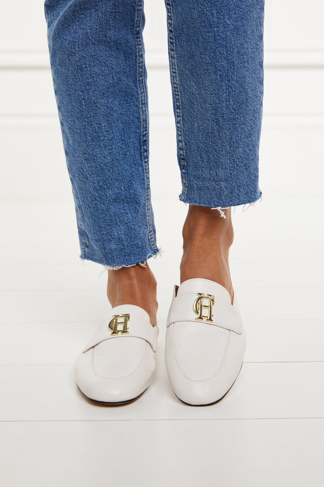 white leather backless loafers with a slightly pointed toe and gold hardware to the top worn with slim denim jeans with a frayed edge