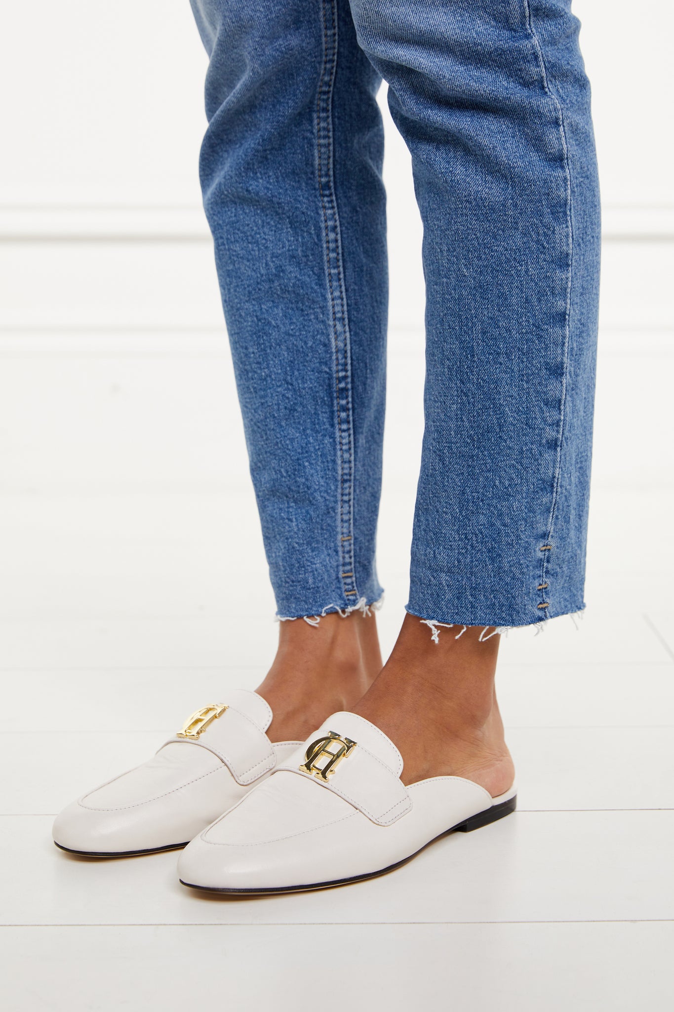 white leather backless loafers with a slightly pointed toe and gold hardware to the top worn with slim denim jeans with a frayed edge
