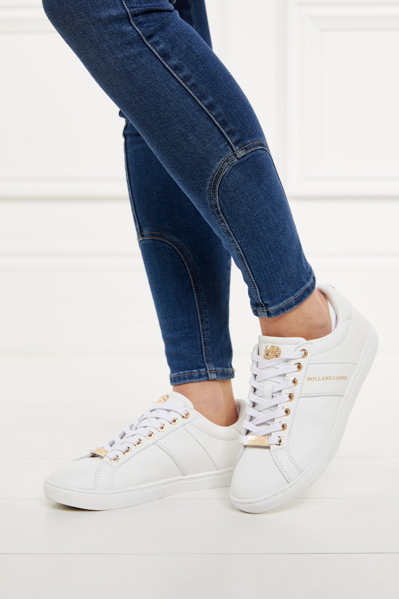 white leather trainers with white laces detailed with gold foil branding on the side and gold hardware. Worn with denim skinny jeans.