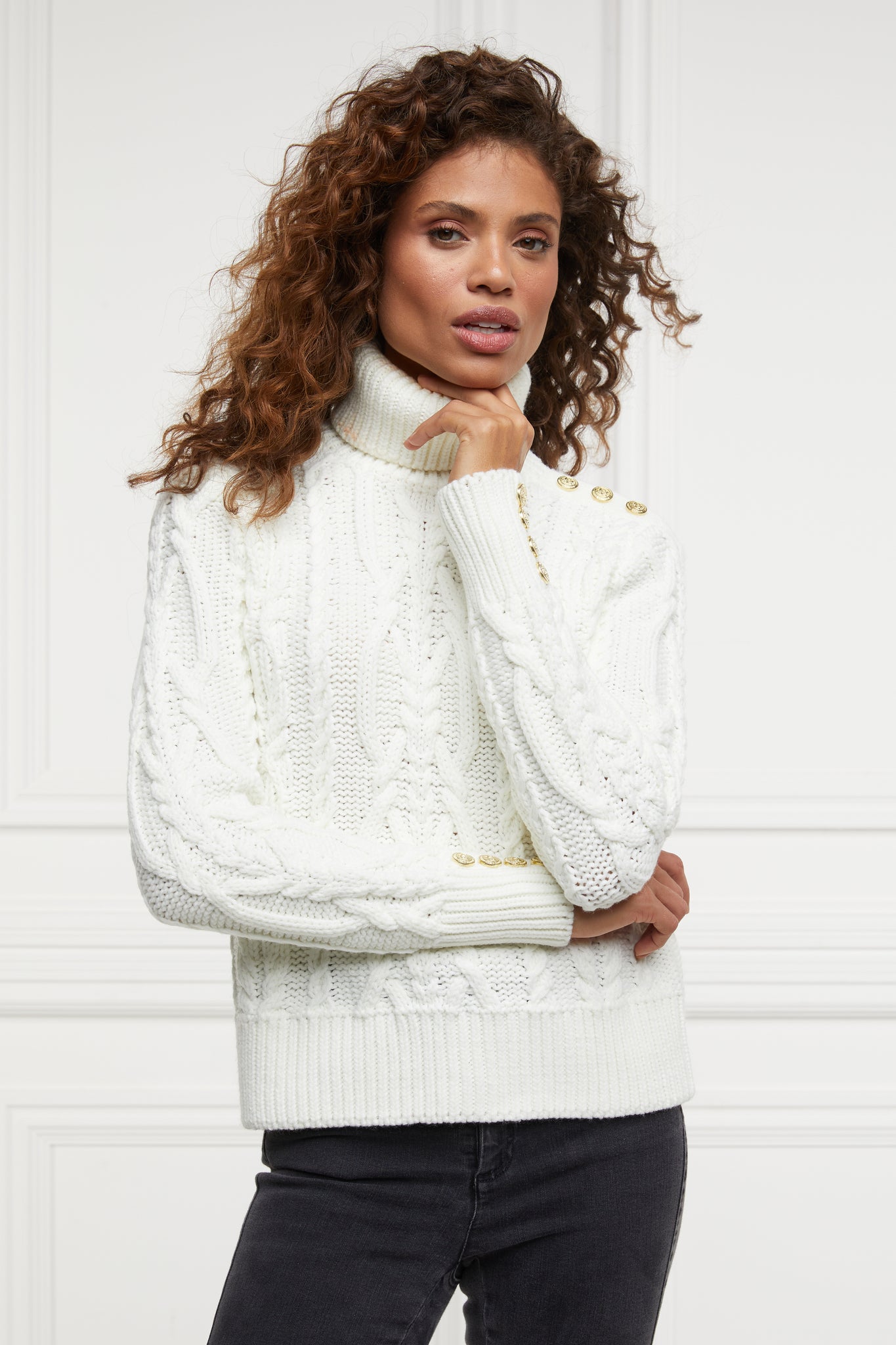 a chunky cable knit roll neck jumper in cream with dropped shoulders and thick ribbed cable trims and gold buttons on cuffs and collar