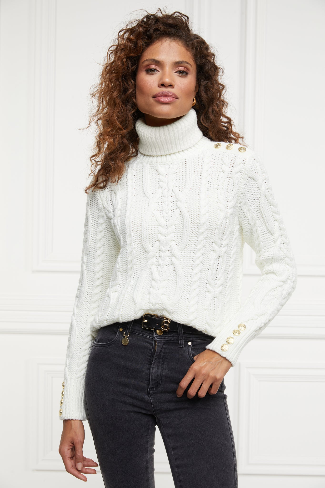 a chunky cable knit roll neck jumper in cream with dropped shoulders and thick ribbed cable trims and gold buttons on cuffs and collar