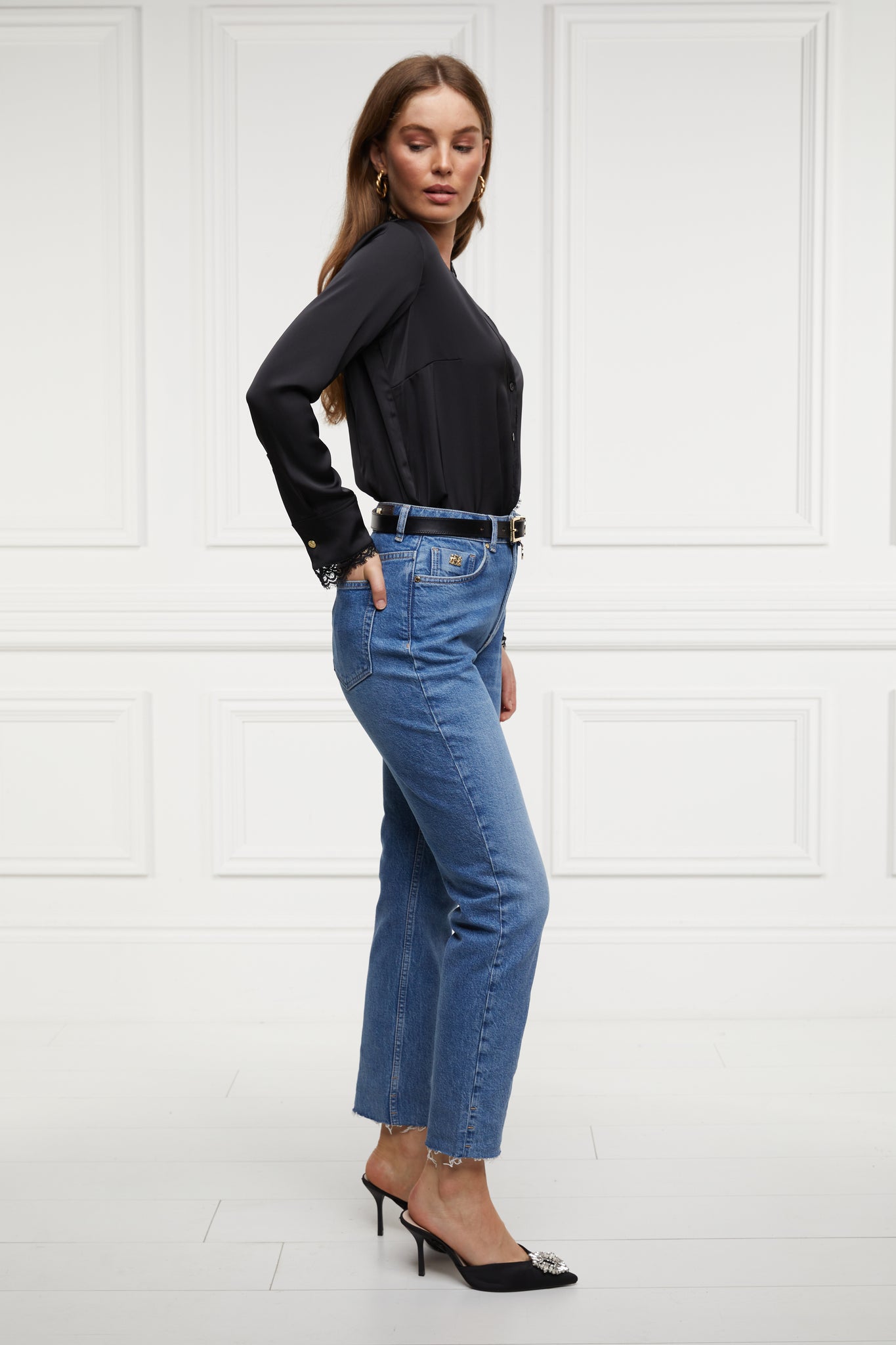 side of womens high rise blue denim slim fit jean with raw hem and two open pockets on the front and back with gold stirrup charm to the belt loop