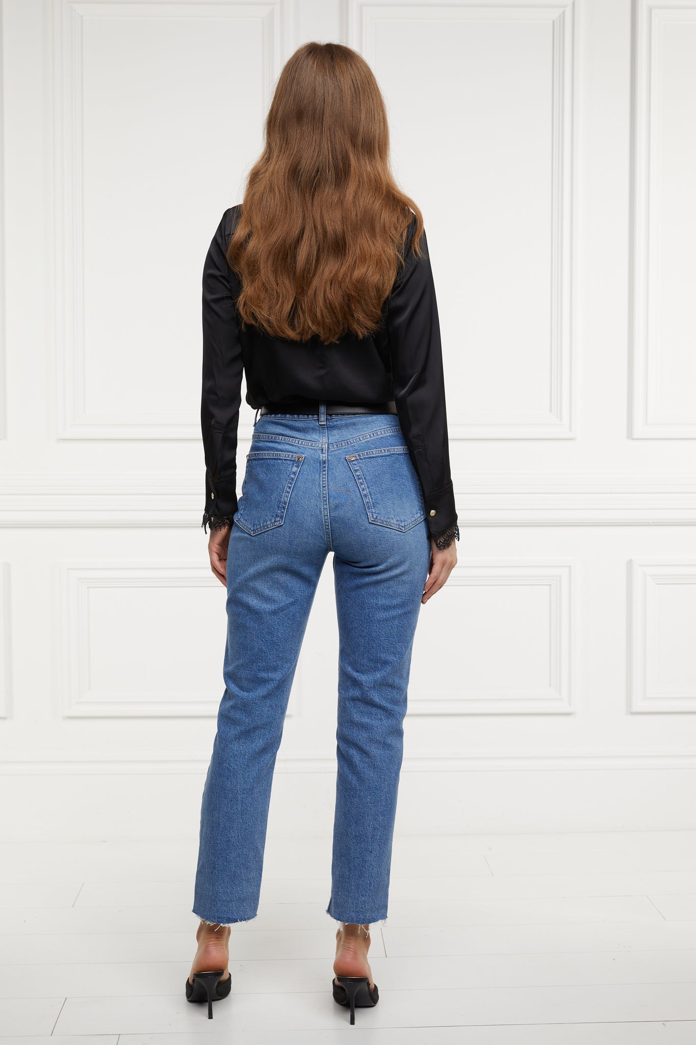 back of womens high rise blue denim slim fit jean with raw hem and two open pockets on the front and back with gold stirrup charm to the belt loop