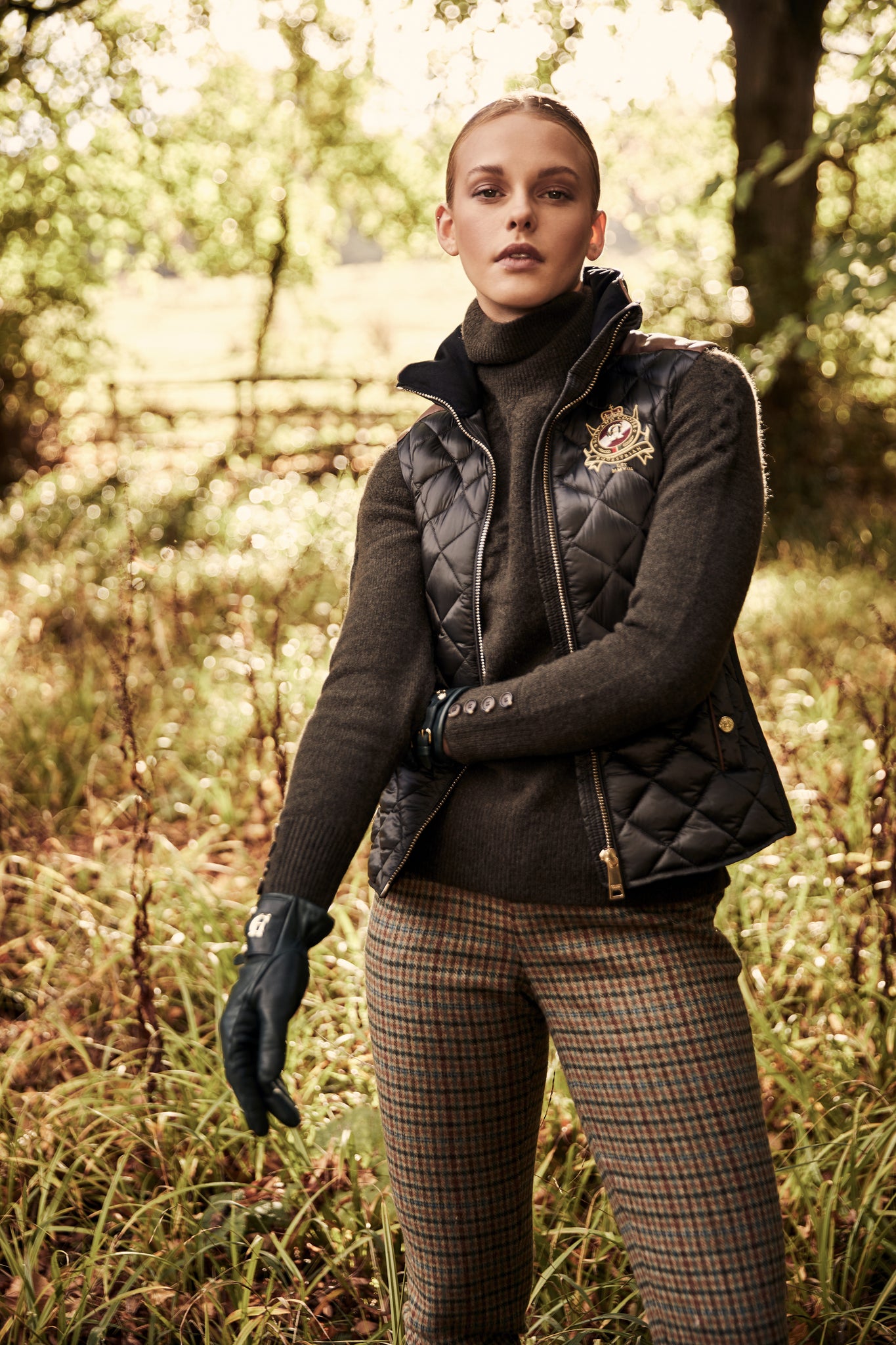 Chunky knit roll neck jumper in fern green layered under a black diamond quilted gilet and worn with black gloves