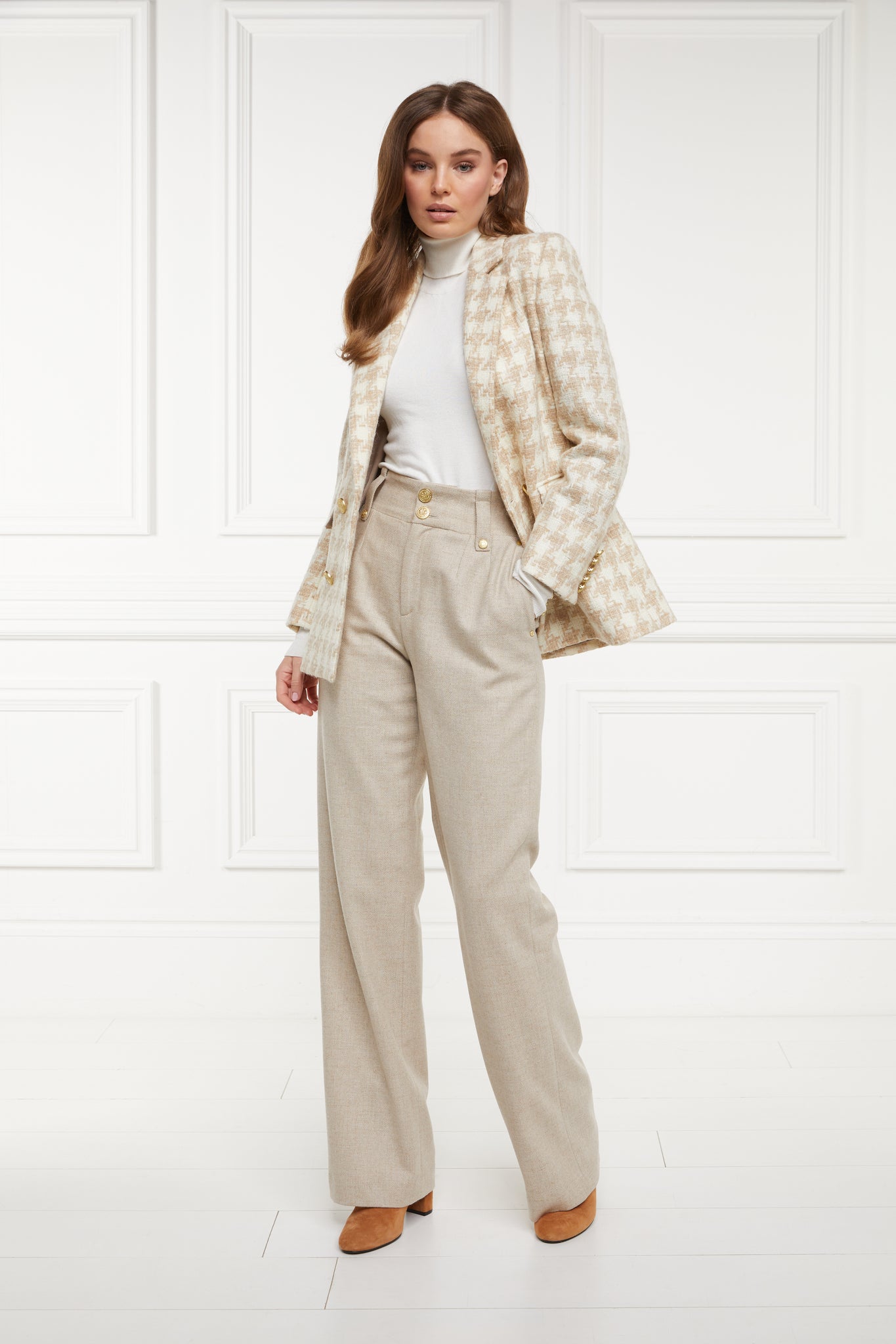 double breasted wool blazer in white and camel houndstooth with two hip pockets and gold button details down front and on cuffs and handmade in the uk worn with white roll neck and beige tailored trousers